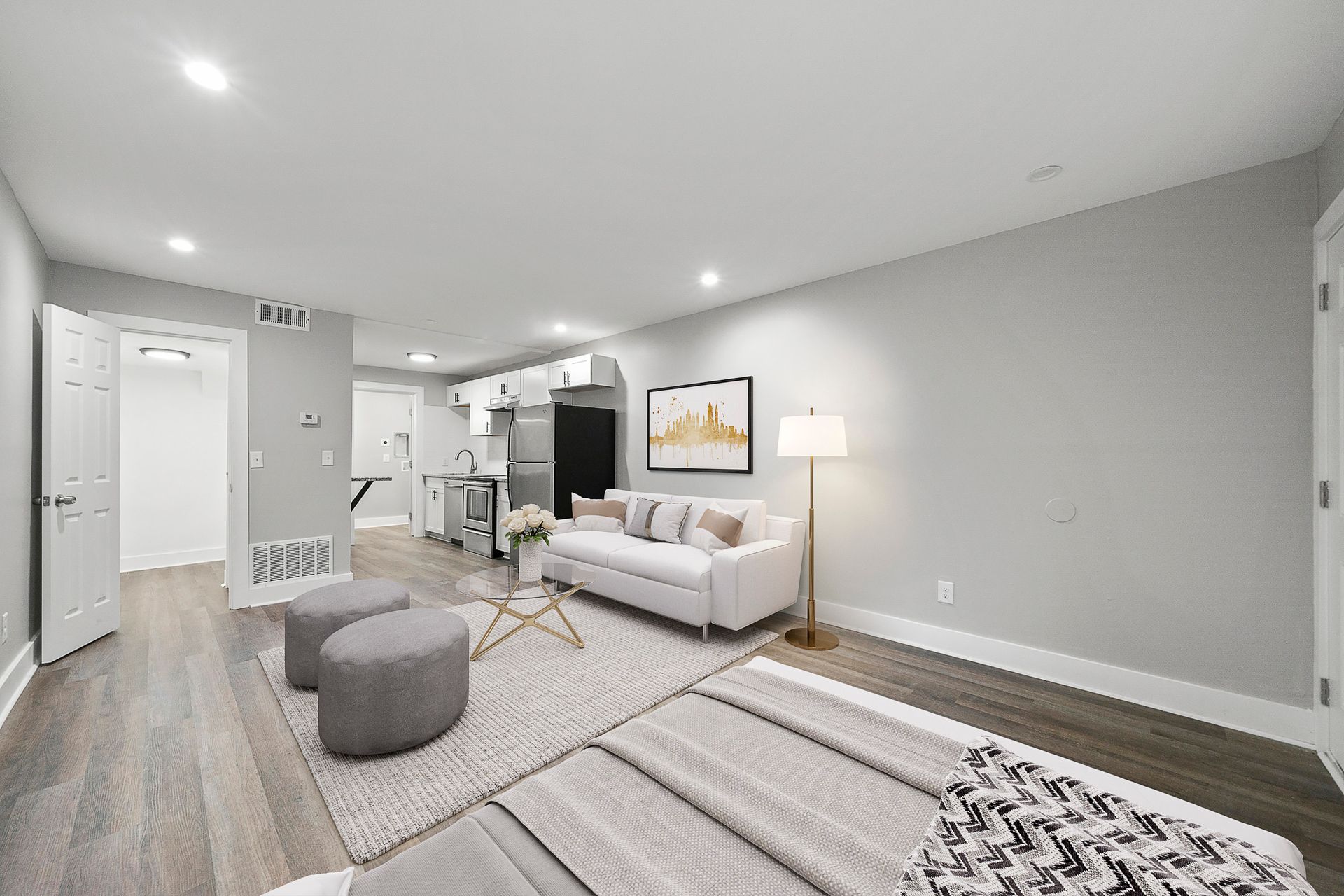 Bright modern living room with sofa, floor lamp, ottoman, and patterned rug on light wood floors.