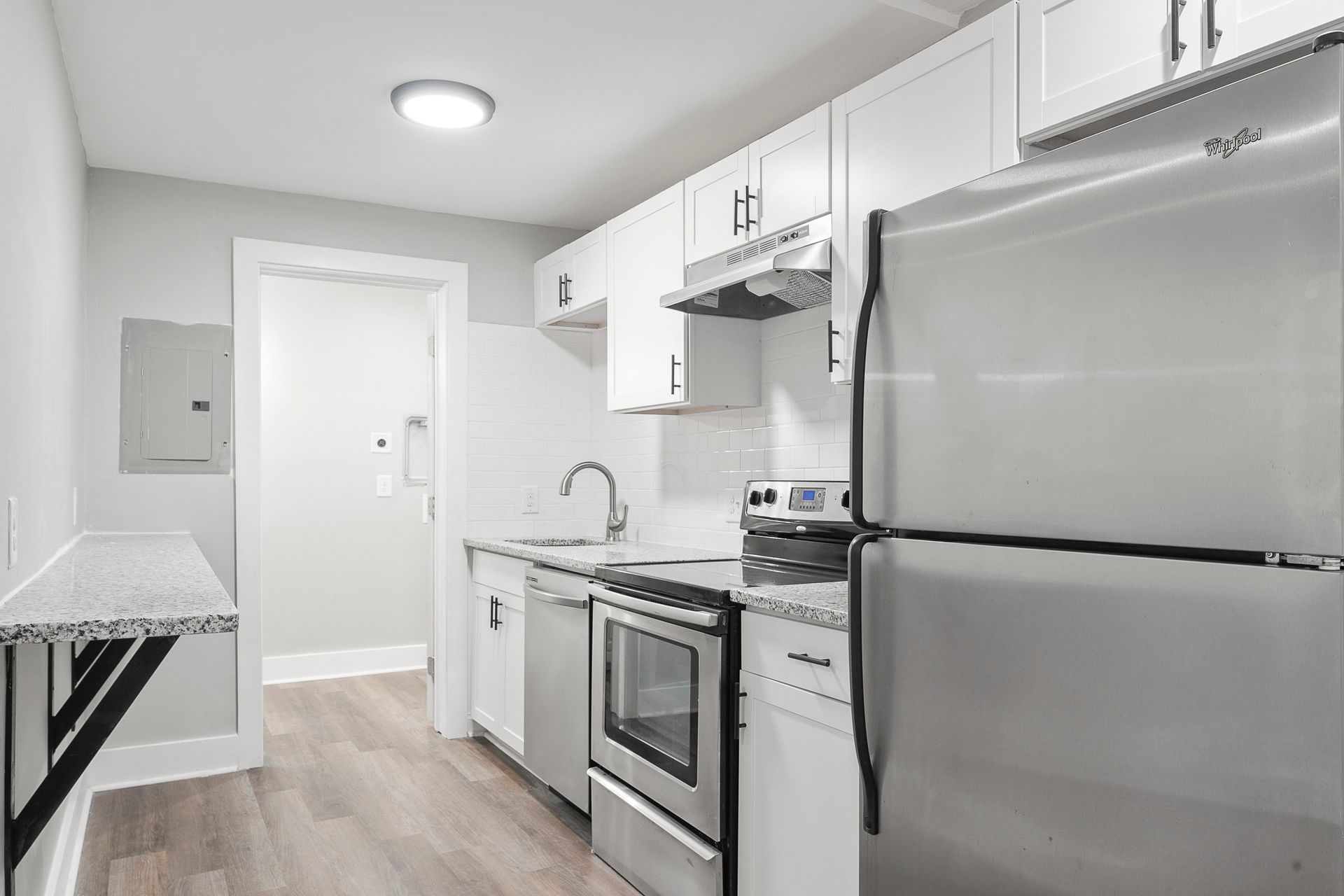 Bright compact kitchen with white cabinets, stainless steel appliances, and light wood flooring