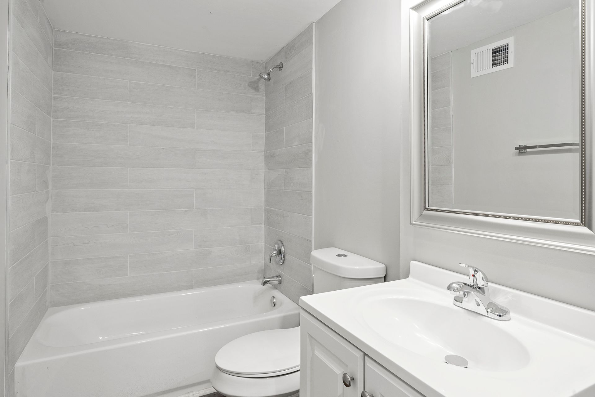 Bright white bathroom with bathtub, toilet, vanity sink, and a large framed mirror