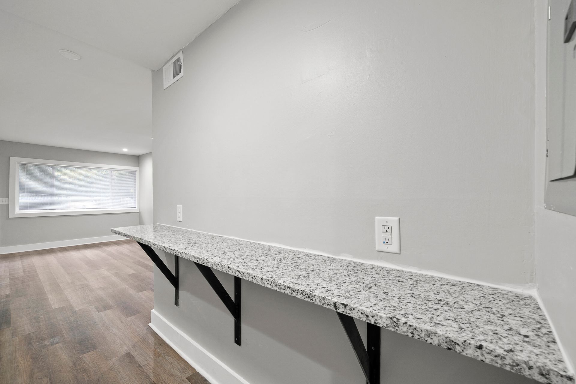 Empty room with a long speckled countertop ledge and black brackets along the wall.