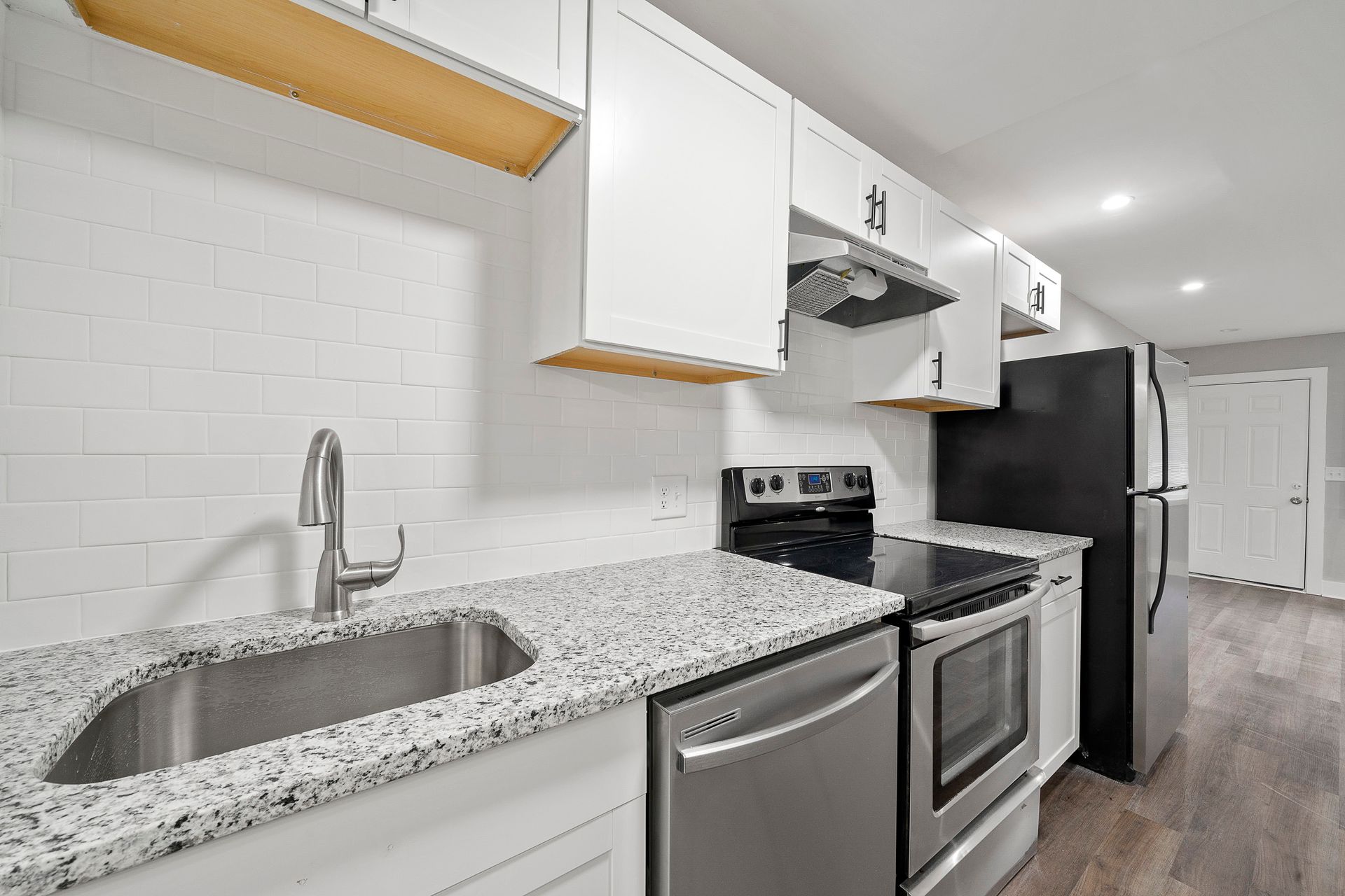 Bright modern kitchen with white cabinets, speckled counters, stainless appliances, and black refrigerator