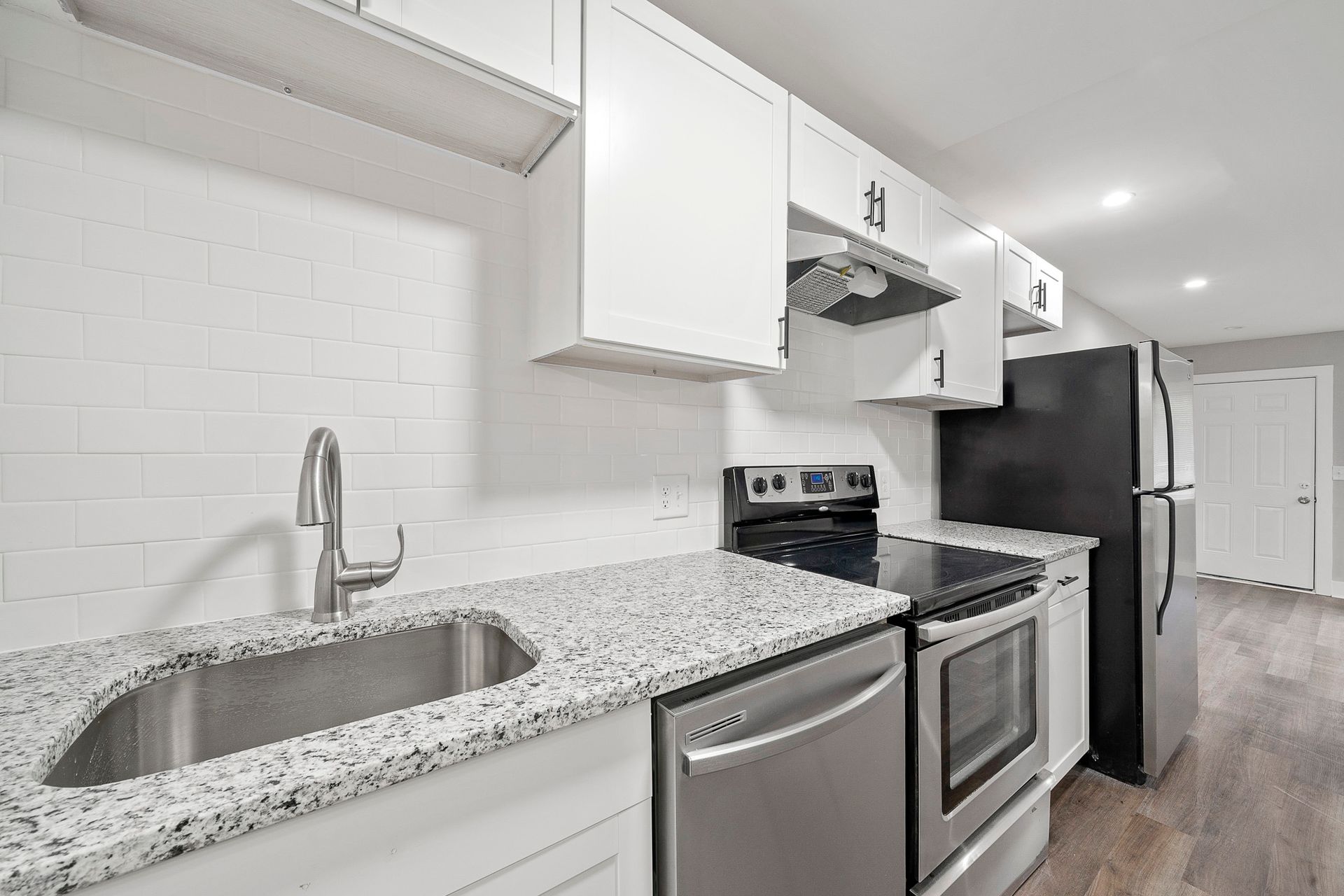 Bright modern kitchen with white cabinets, granite counters, stainless appliances, and a black refrigerator.