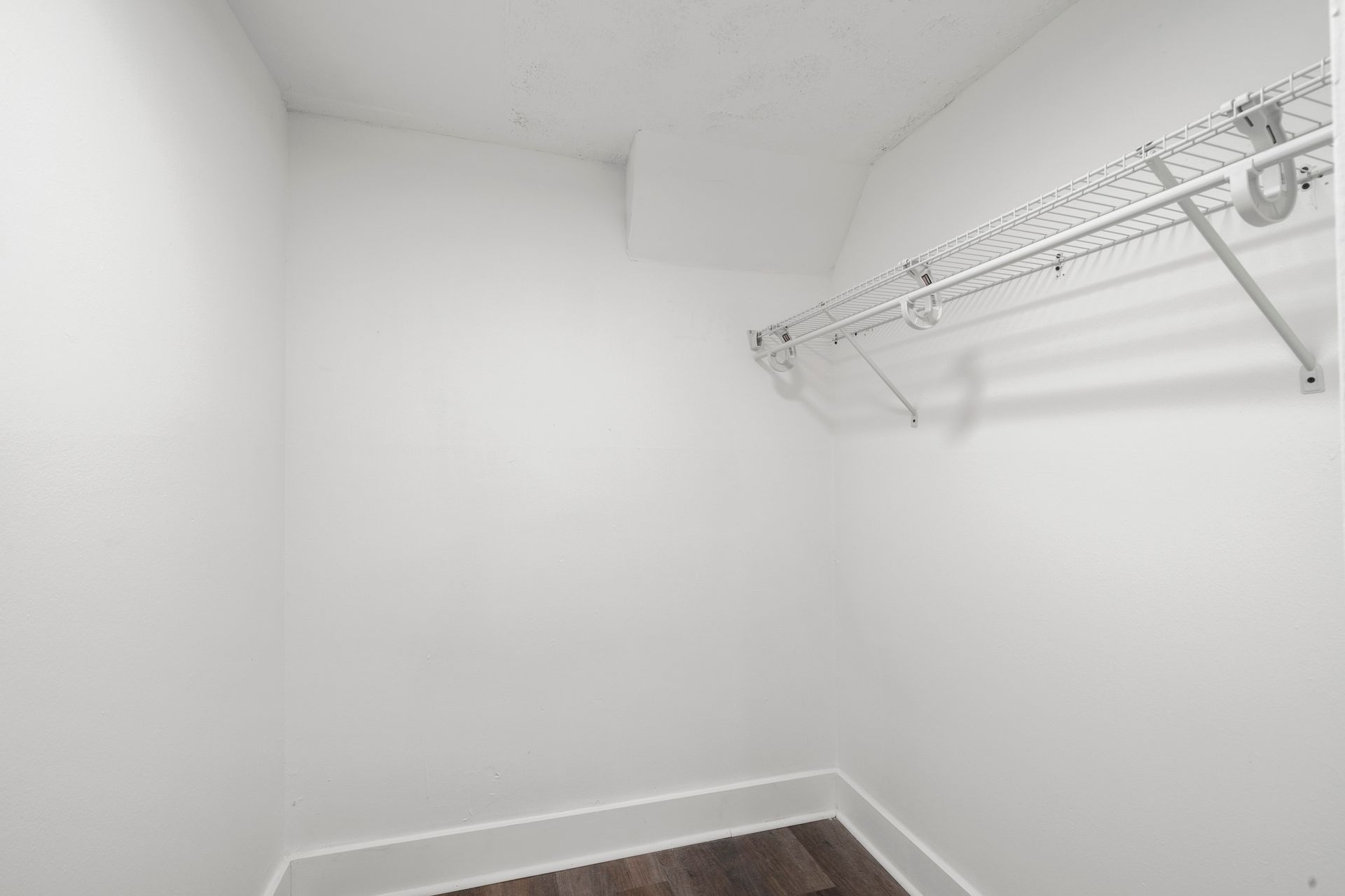 Empty white closet with wire shelving and dark wood floor