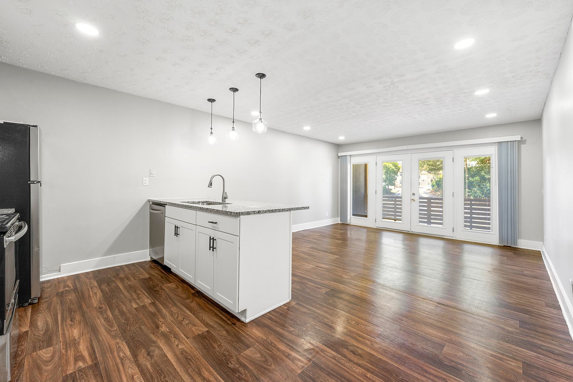 Bright open kitchen and living area with dark wood floors, white island, and French doors to a patio