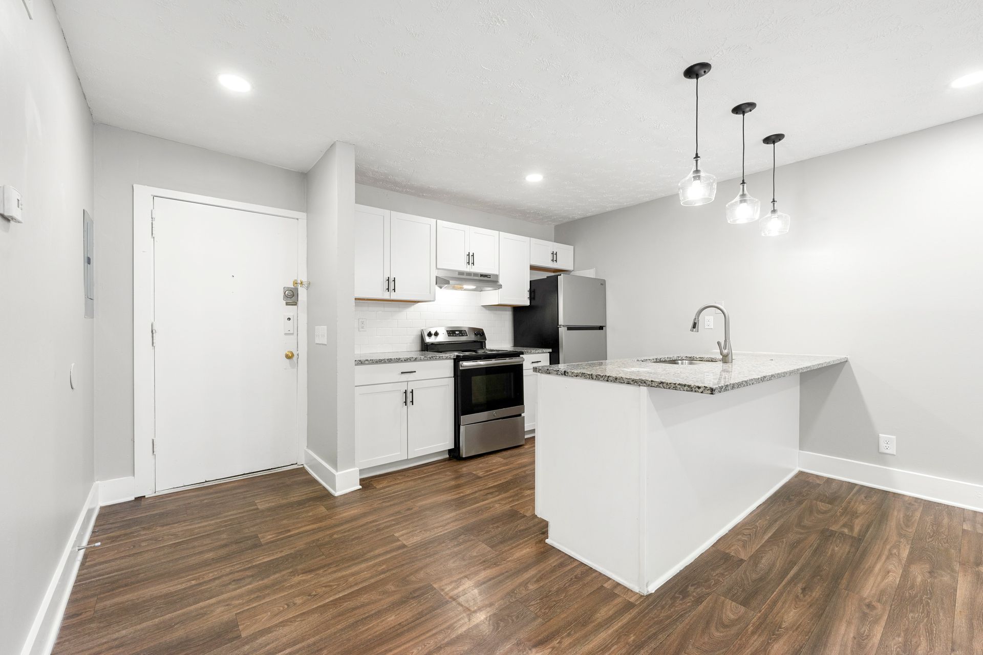 Modern open kitchen with white cabinets, stainless appliances, granite island, and wood flooring