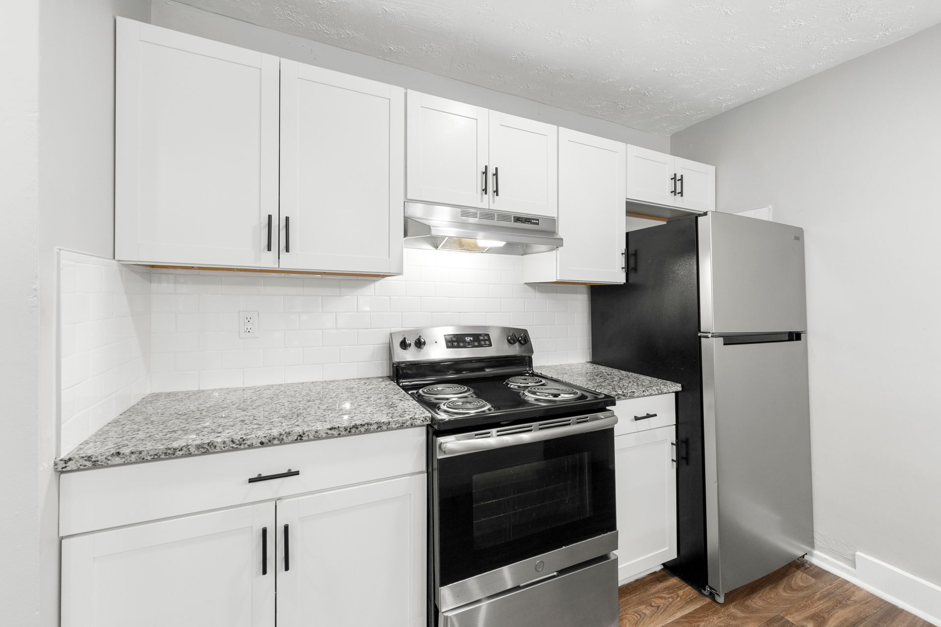 Bright white kitchen with granite countertops, stainless steel stove and refrigerator, and white cabinets.