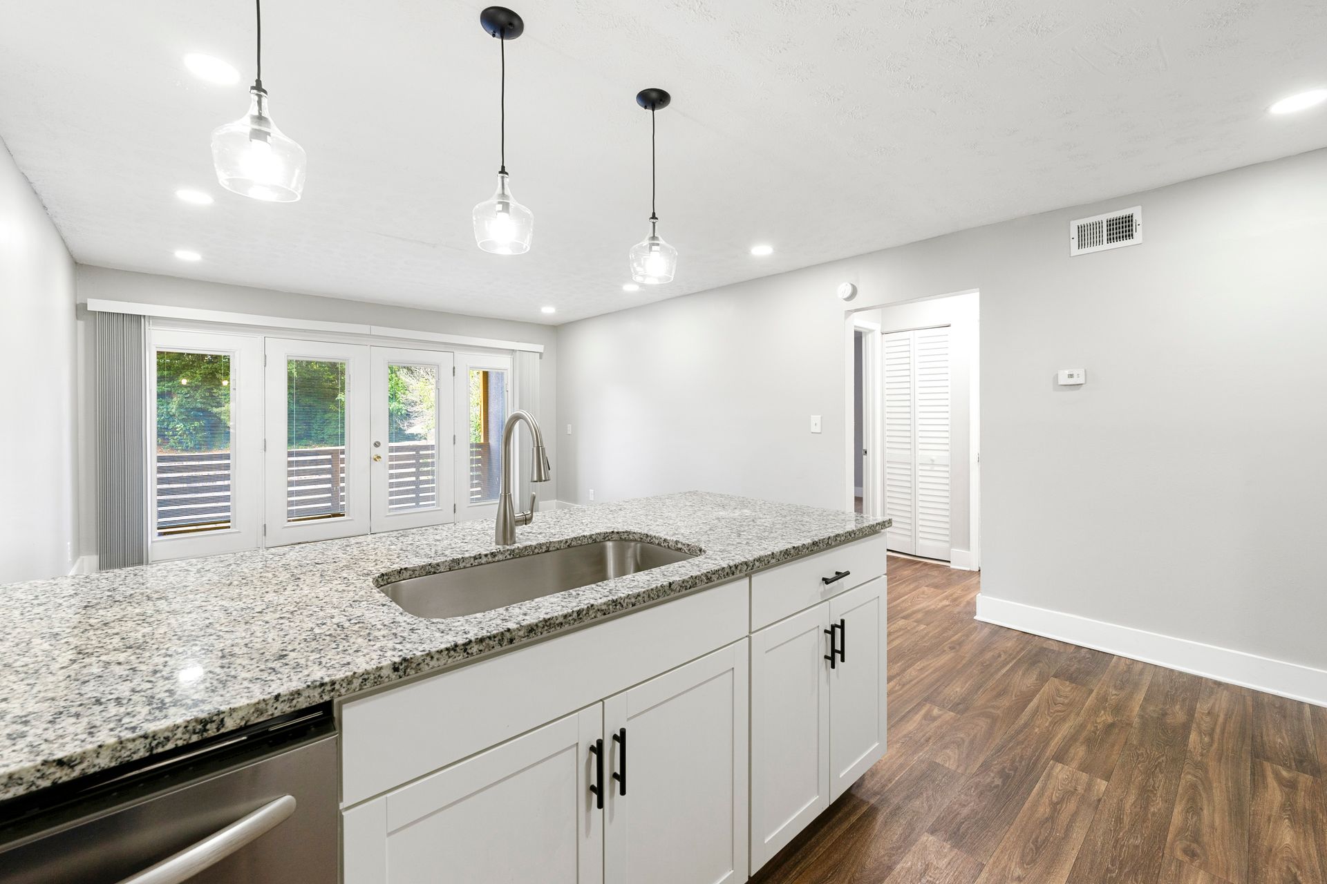 Modern white kitchen with granite island, pendant lights, wood floors, and bright windows