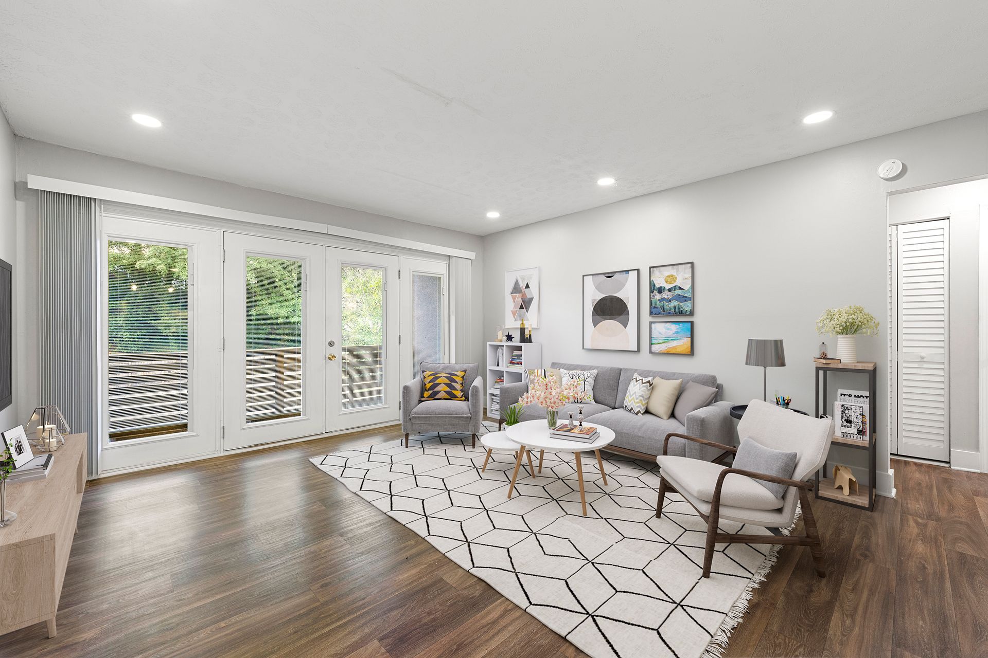 Bright living room with gray sofa, patterned rug, wall art, and large windows overlooking greenery