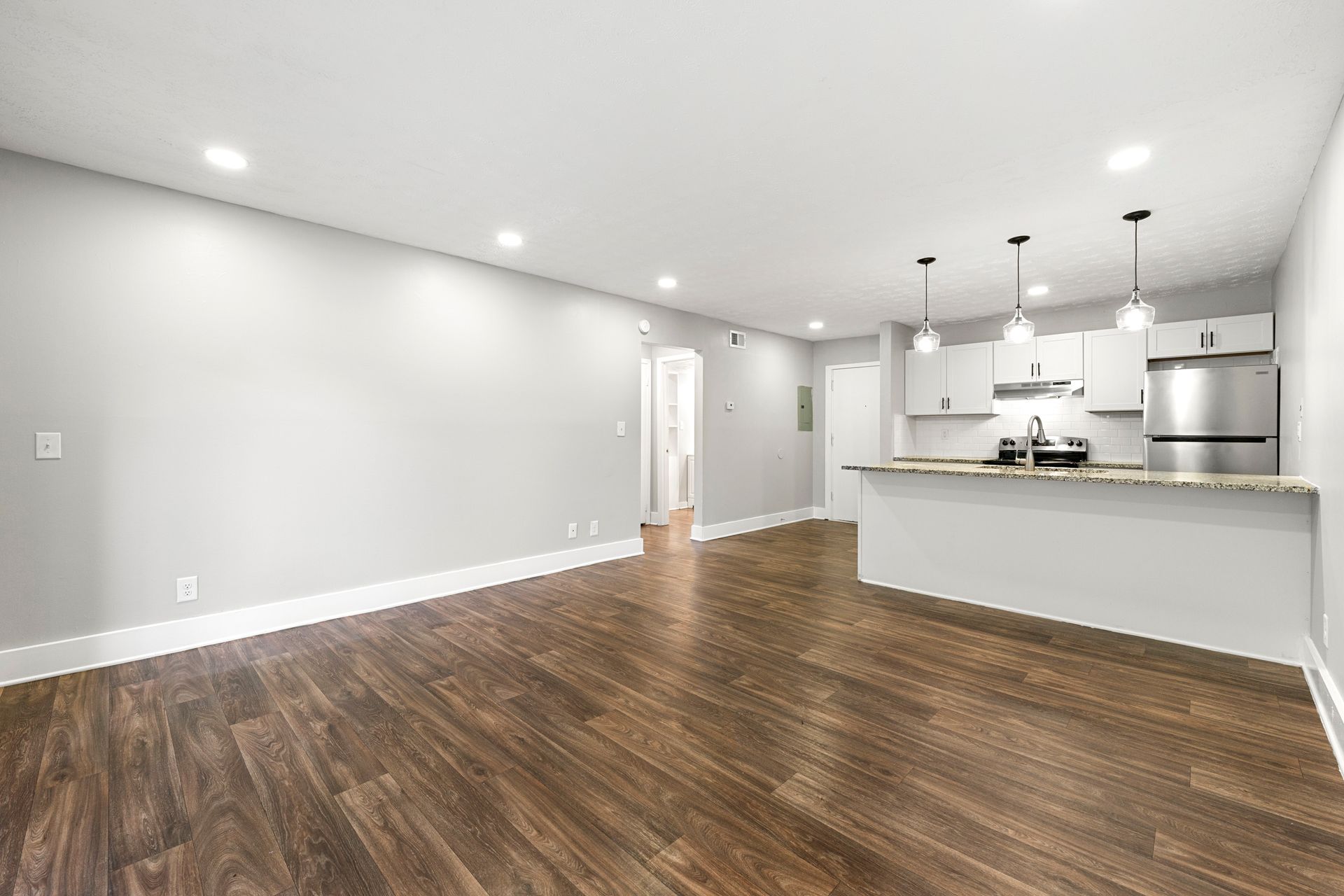 Empty modern kitchen and living area with wood floors, white walls, and a large island