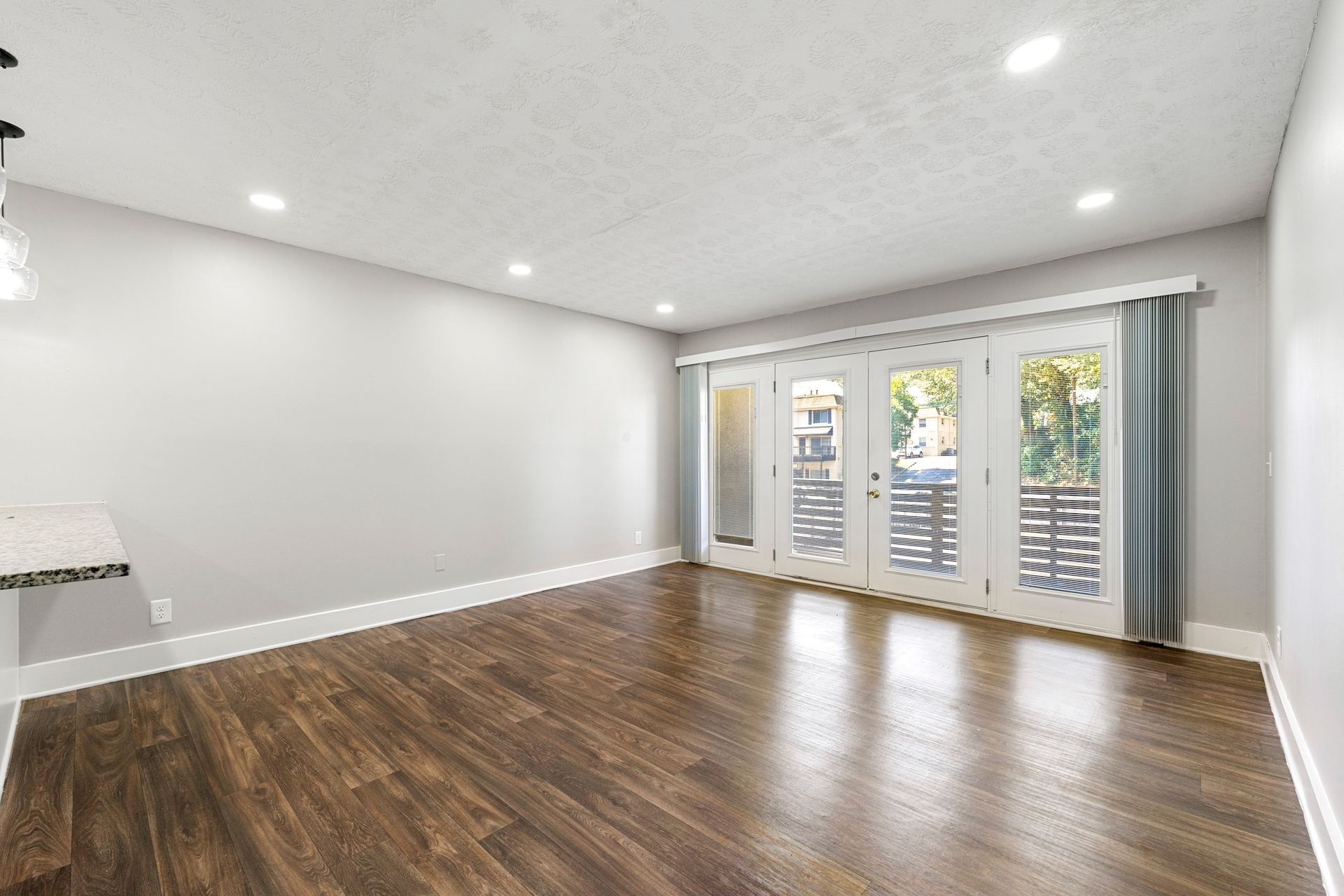 Spacious empty living room with hardwood floors, white walls, and sliding glass doors with curtains.