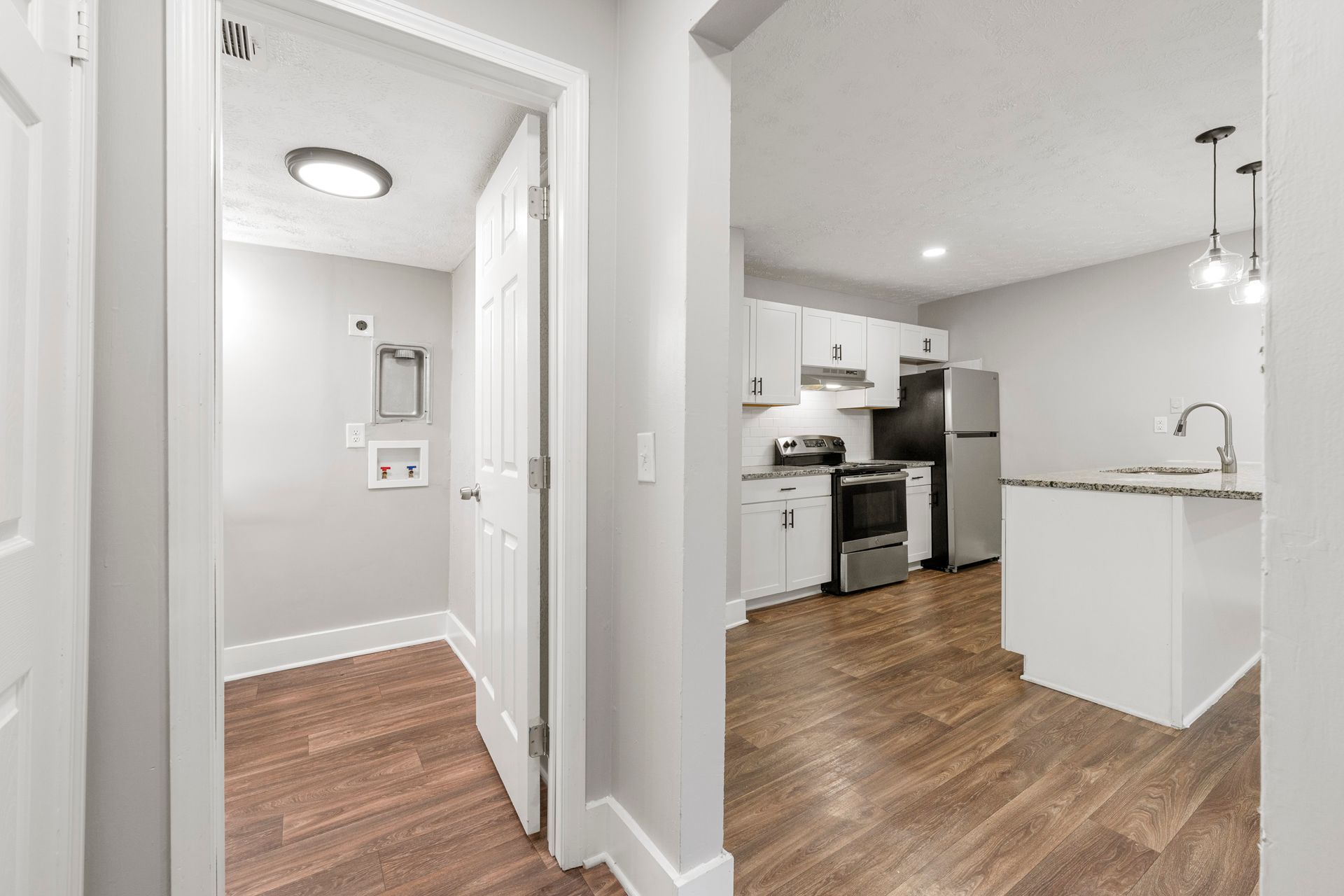 Hallway leading to a bright kitchen with white cabinets, stainless appliances, and wood floors
