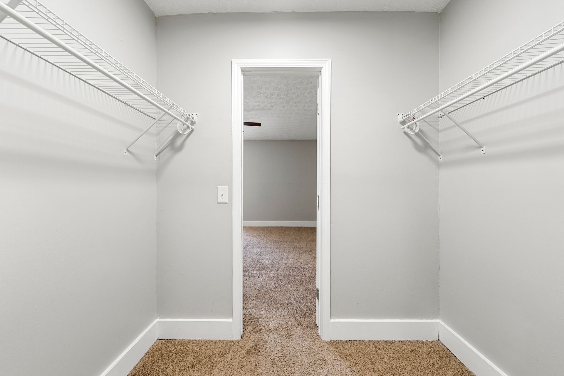 Empty walk-in closet with white wire shelving and beige carpet, viewed through an open doorway.