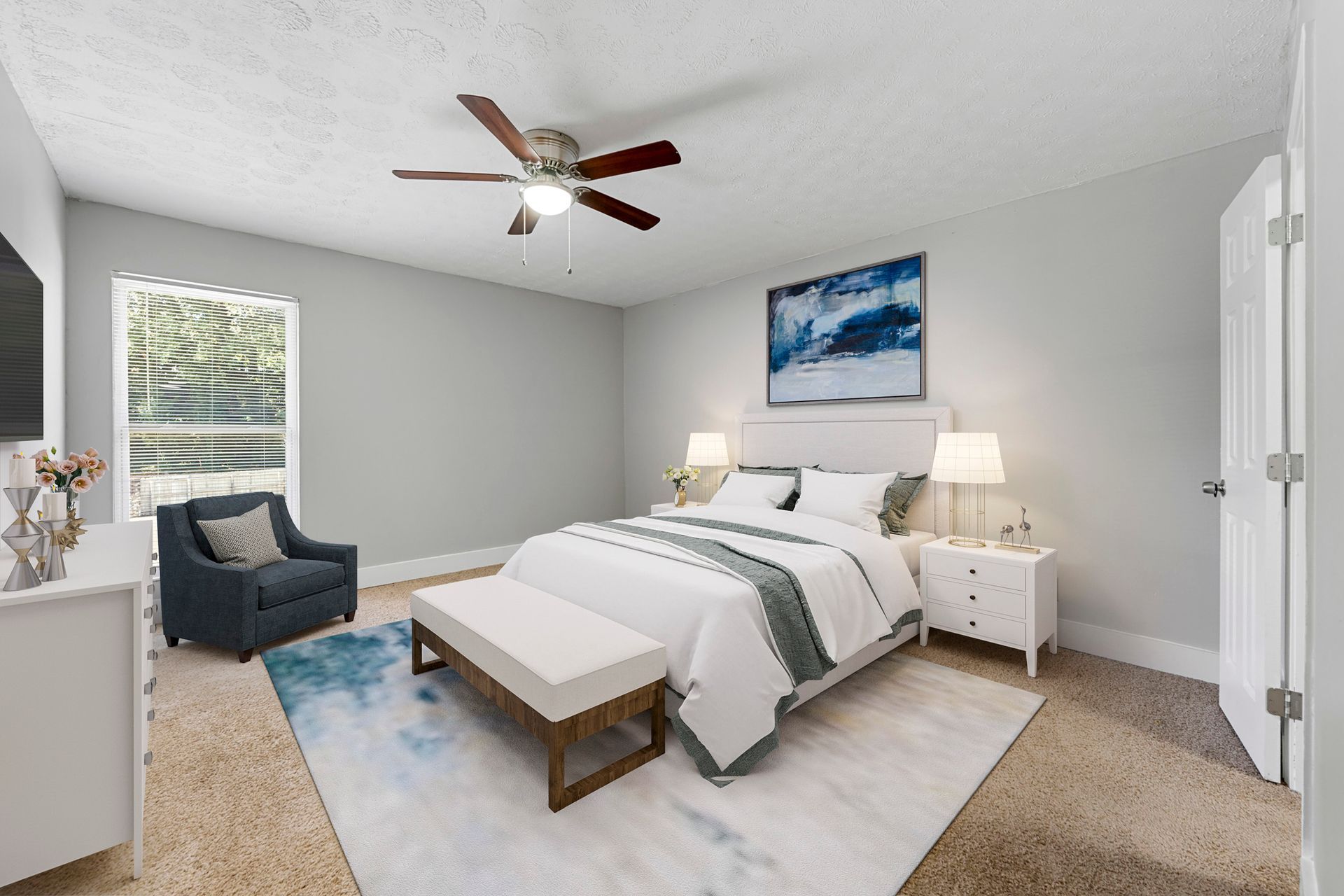 Bright gray bedroom with a king bed, blue chair, white nightstands, and ceiling fan