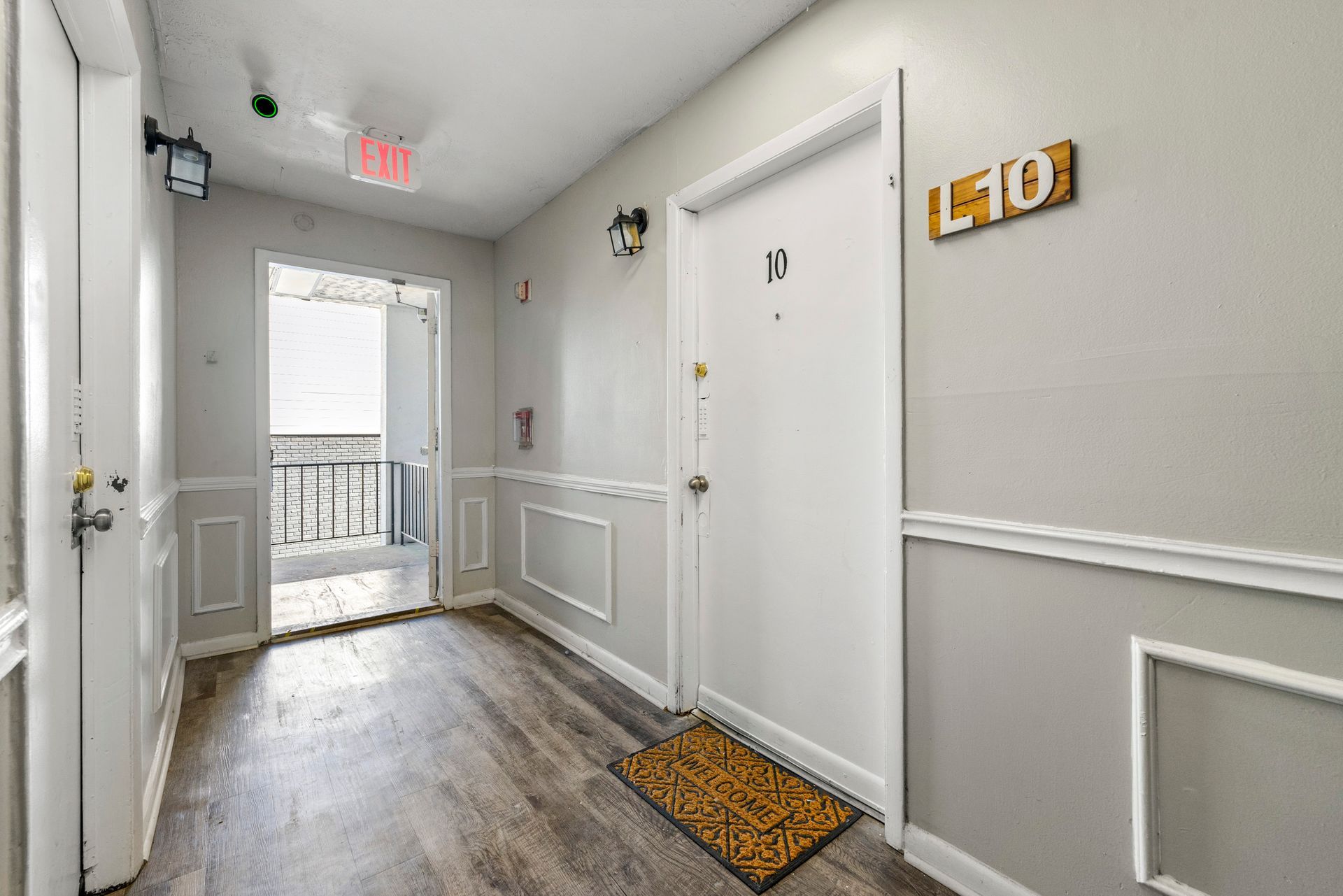 Bright apartment hallway with white doors, wall molding, wood floor, and a balcony door at the end.