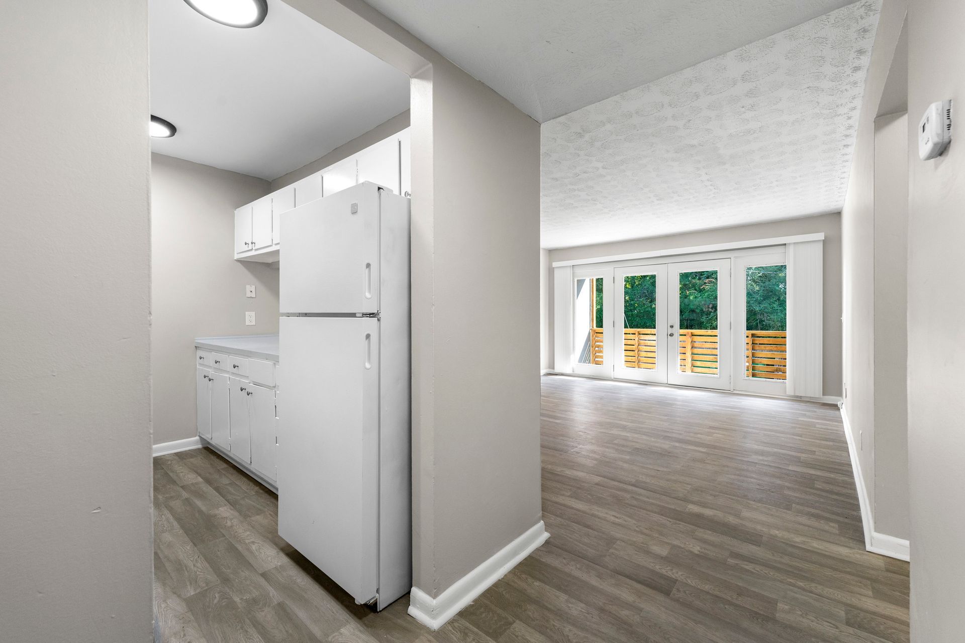 Empty kitchen and dining area with white cabinets, gray flooring, and a bright window view