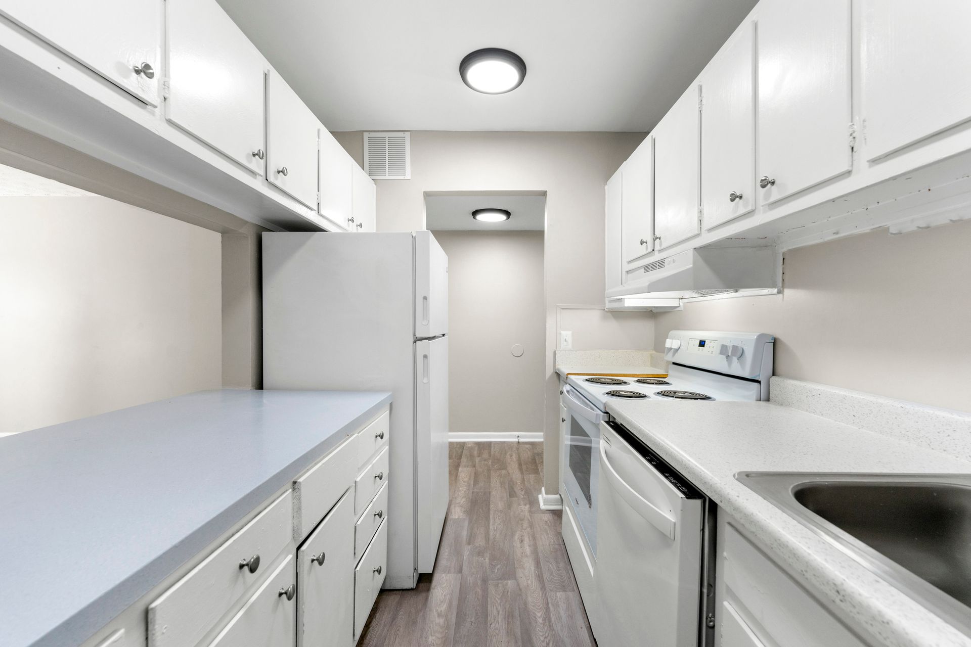 Bright white galley kitchen with white cabinets, stove, refrigerator, and sink.