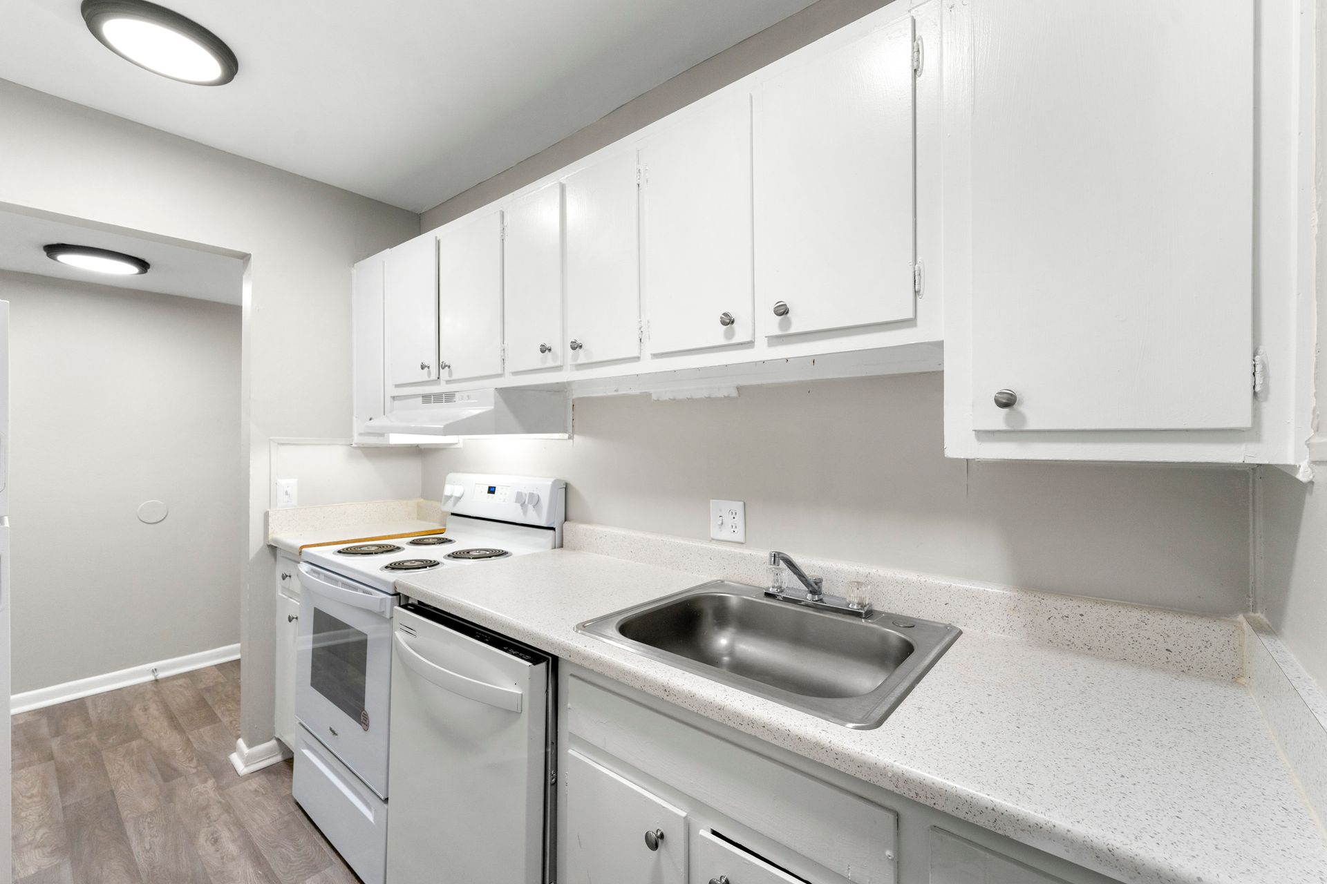 Bright white kitchen with cabinets, stove, dishwasher, and sink along one wall