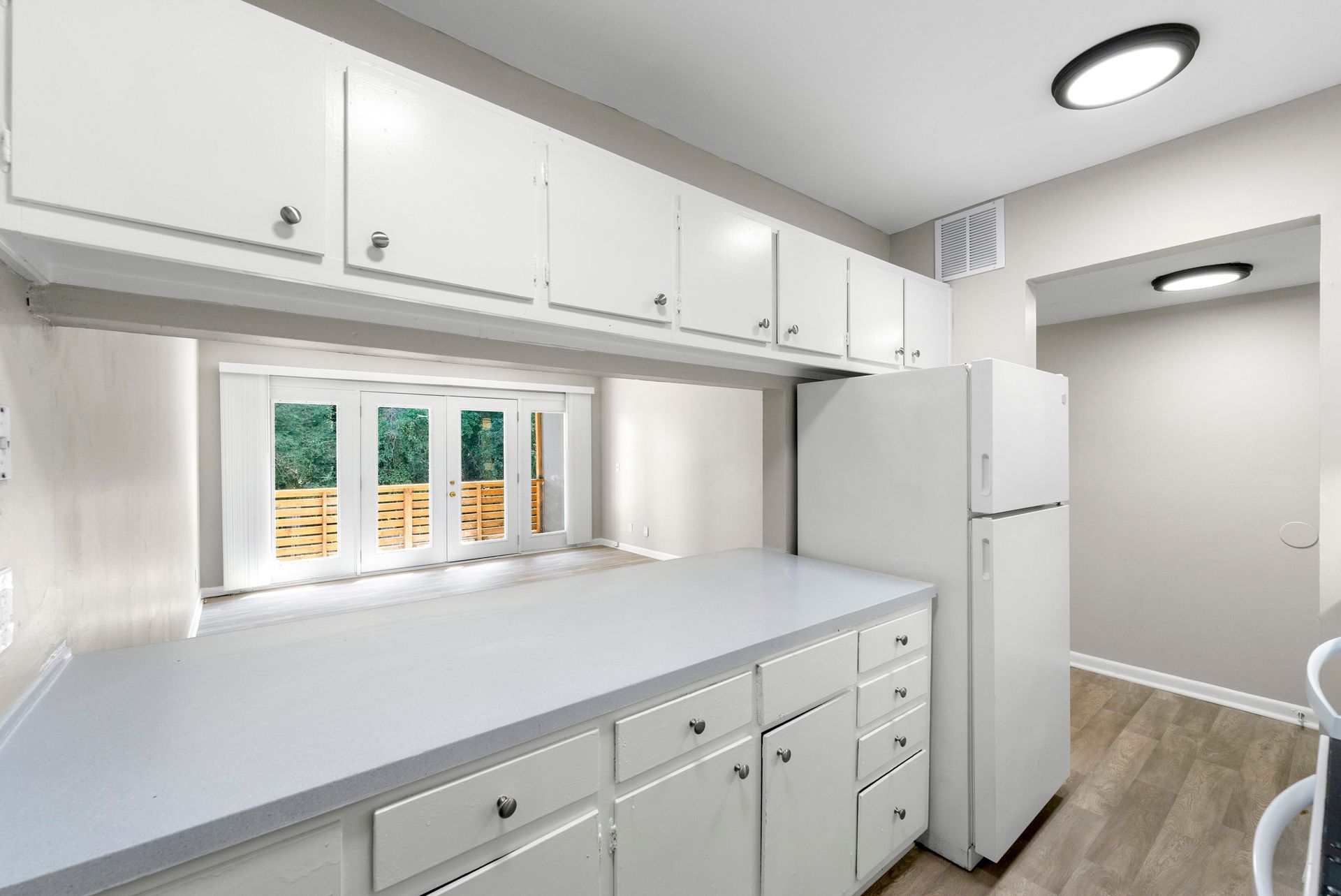 Bright white kitchen with cabinets, countertop, window, and refrigerator