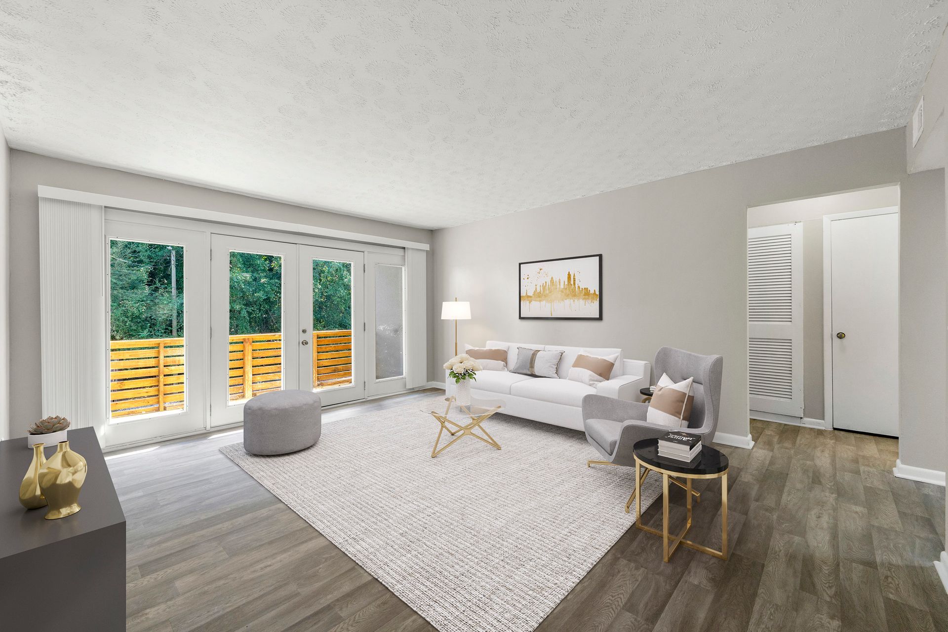 Bright modern living room with gray sofa, white rug, wood floors, and large windows overlooking greenery