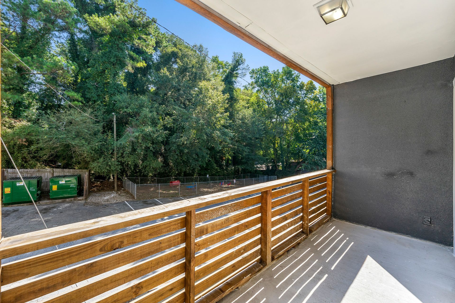 Apartment balcony with wood railing overlooking trees and a green dumpster area