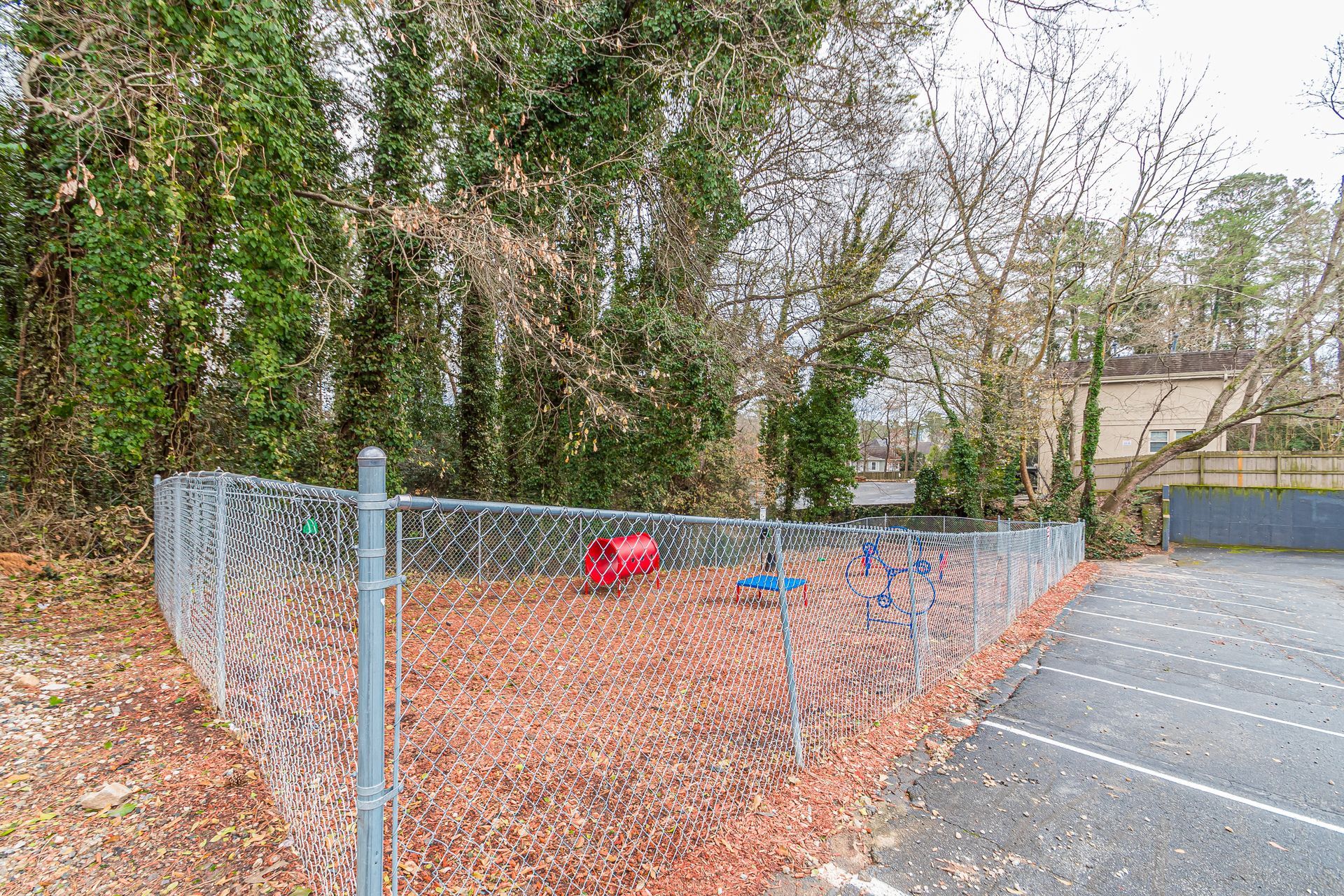 Chain-link fenced parking lot beside trees with a red cart and blue post near the curb