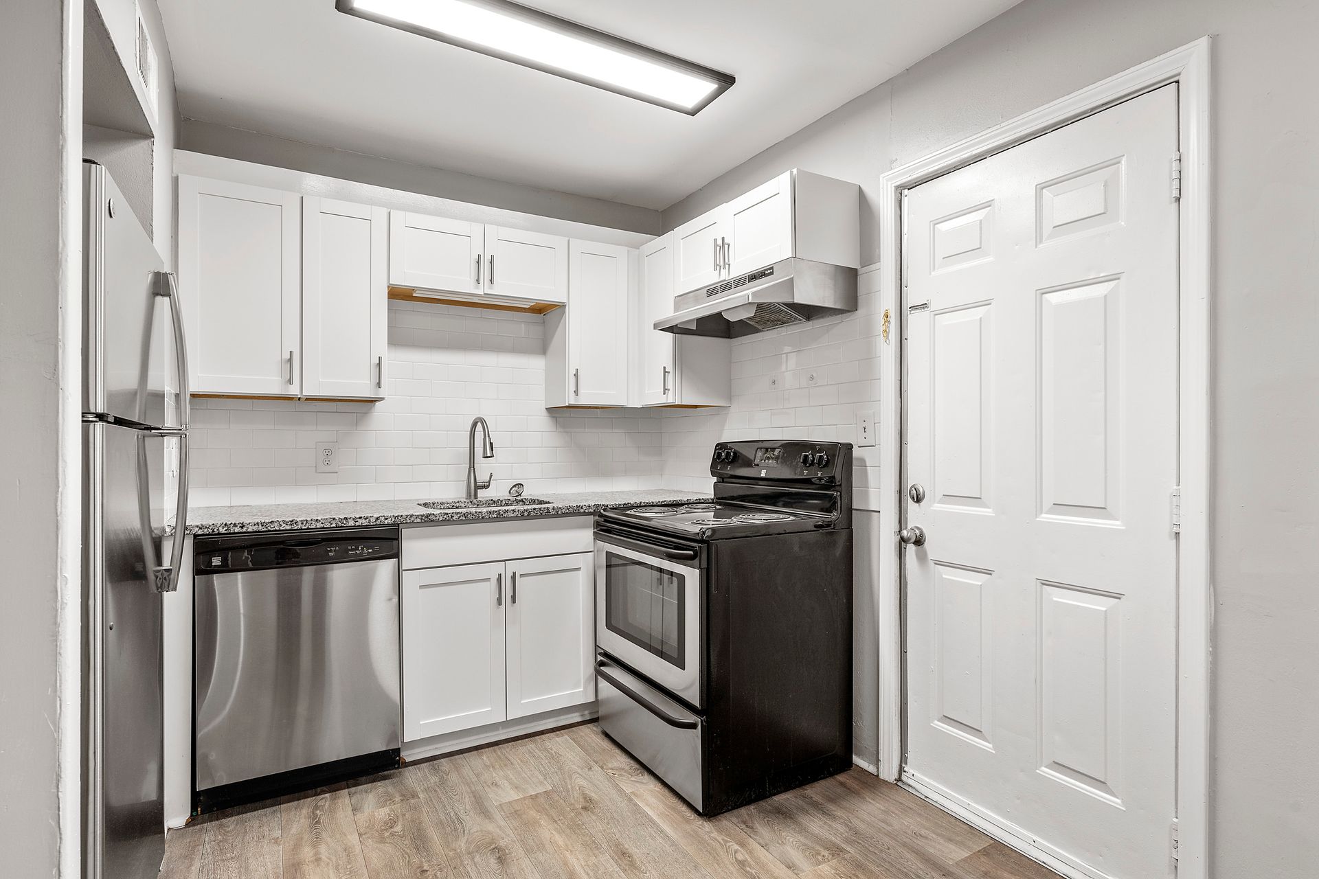 Bright white compact kitchen with stainless steel appliances and black stove