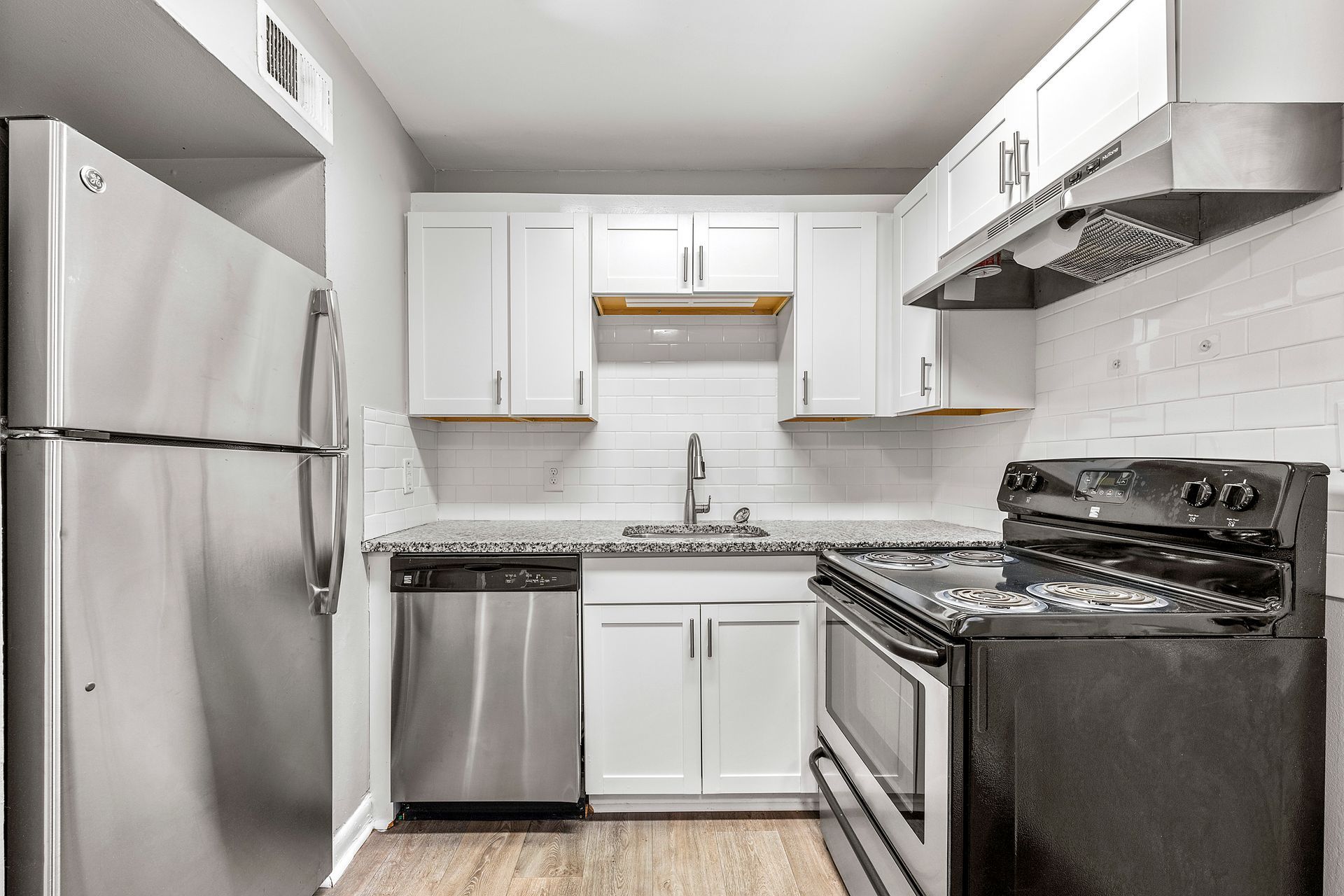 Compact white kitchen with stainless steel appliances, black stove, and white cabinets