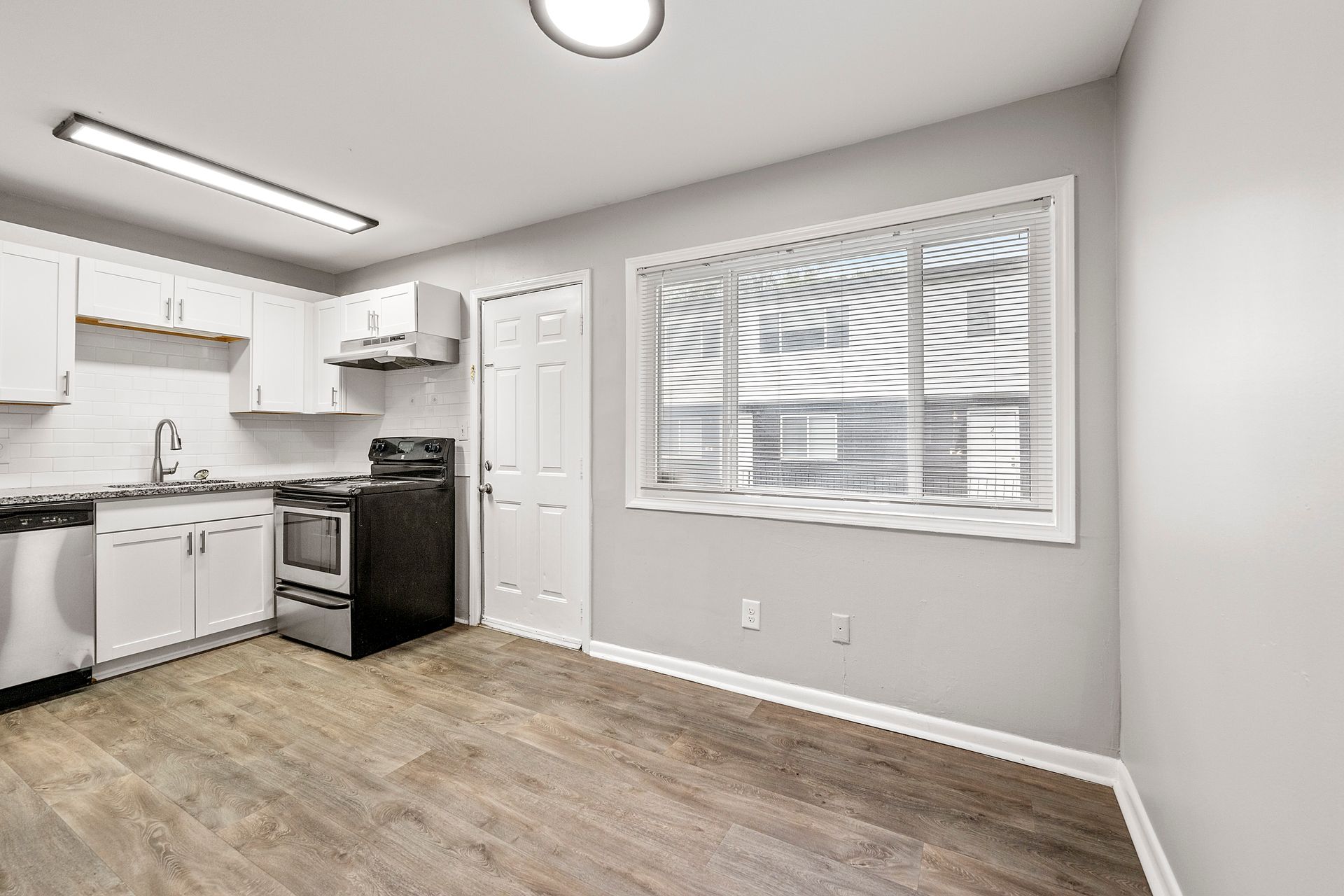 Empty modern kitchen with white cabinets, stove, sink, and a large window on light wood flooring