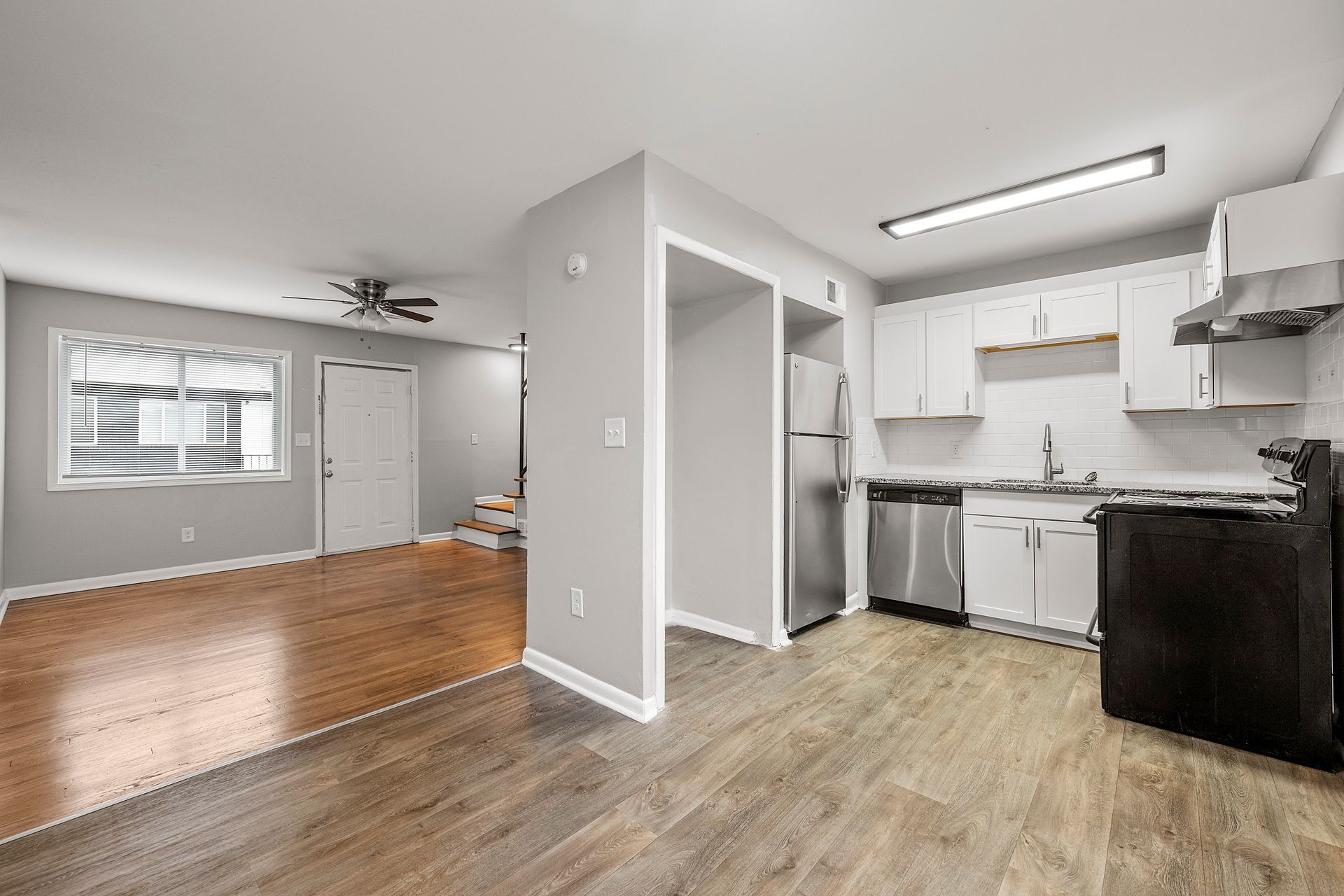 Open-plan apartment with kitchen, wood flooring, and bright living area leading to a staircase.