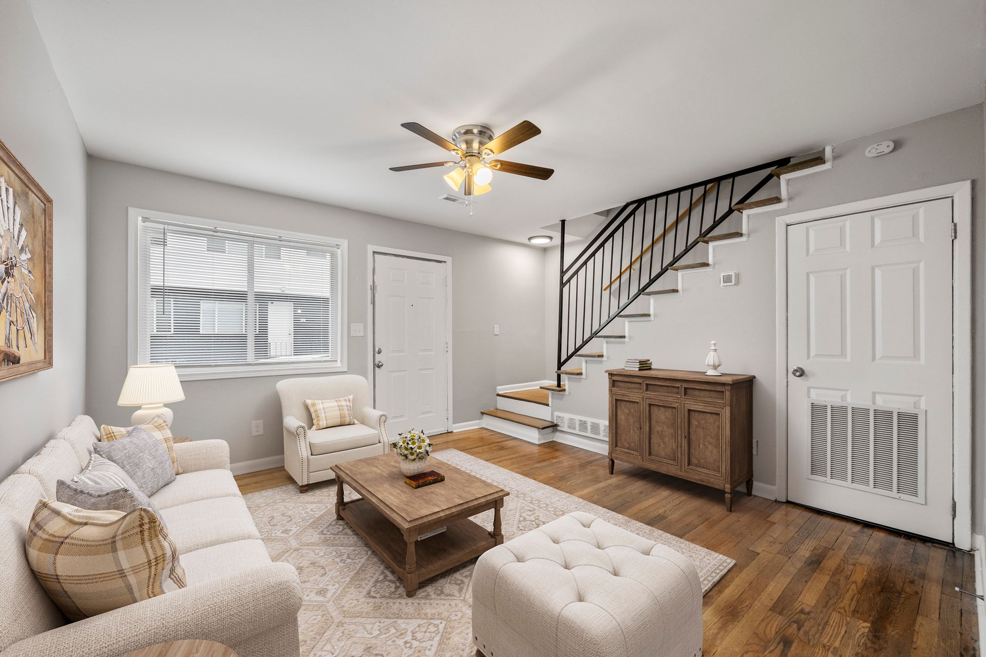 Bright living room with white sofa, armchair, coffee table, staircase, and wood floors