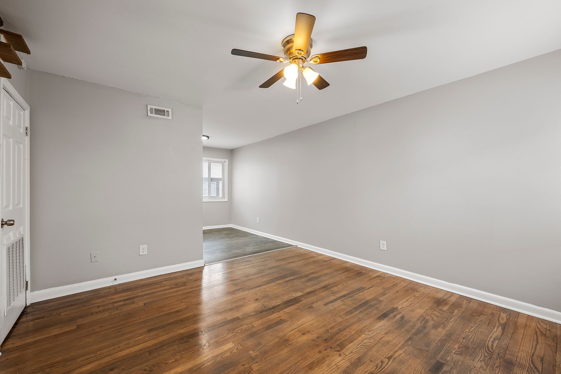 Empty room with hardwood floors, gray walls, and a ceiling fan with lights.