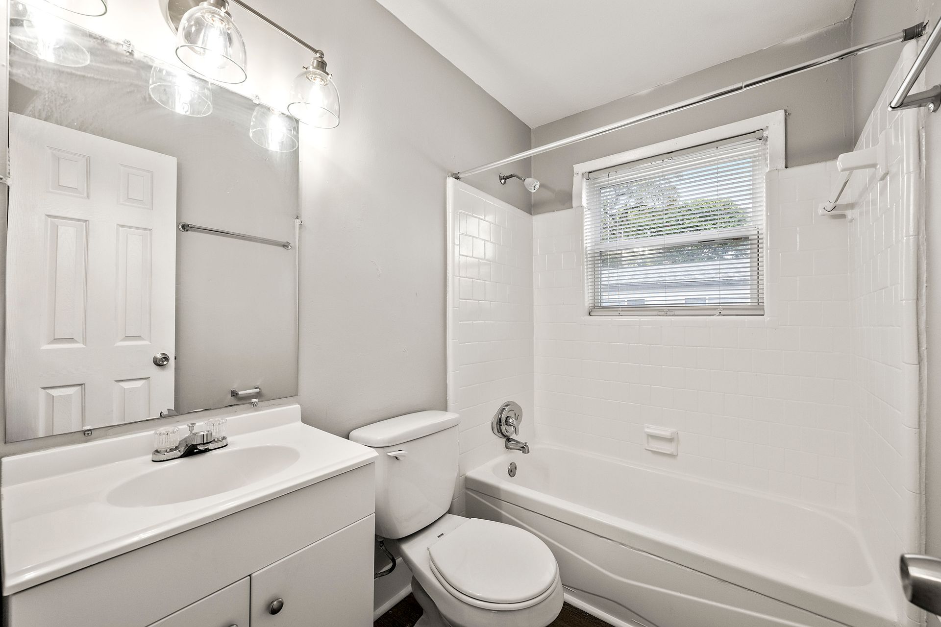 Bright white bathroom with sink, toilet, bathtub, mirror, and window blinds