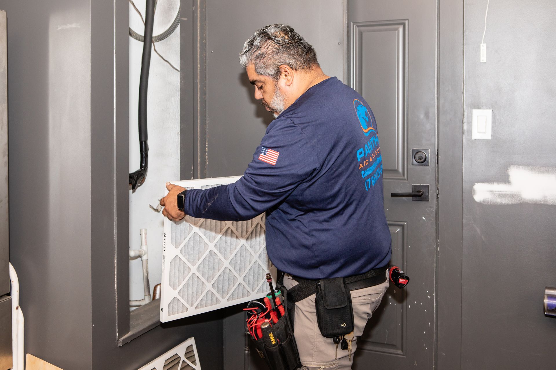 Technician installing or inspecting a wall vent in a gray interior entryway