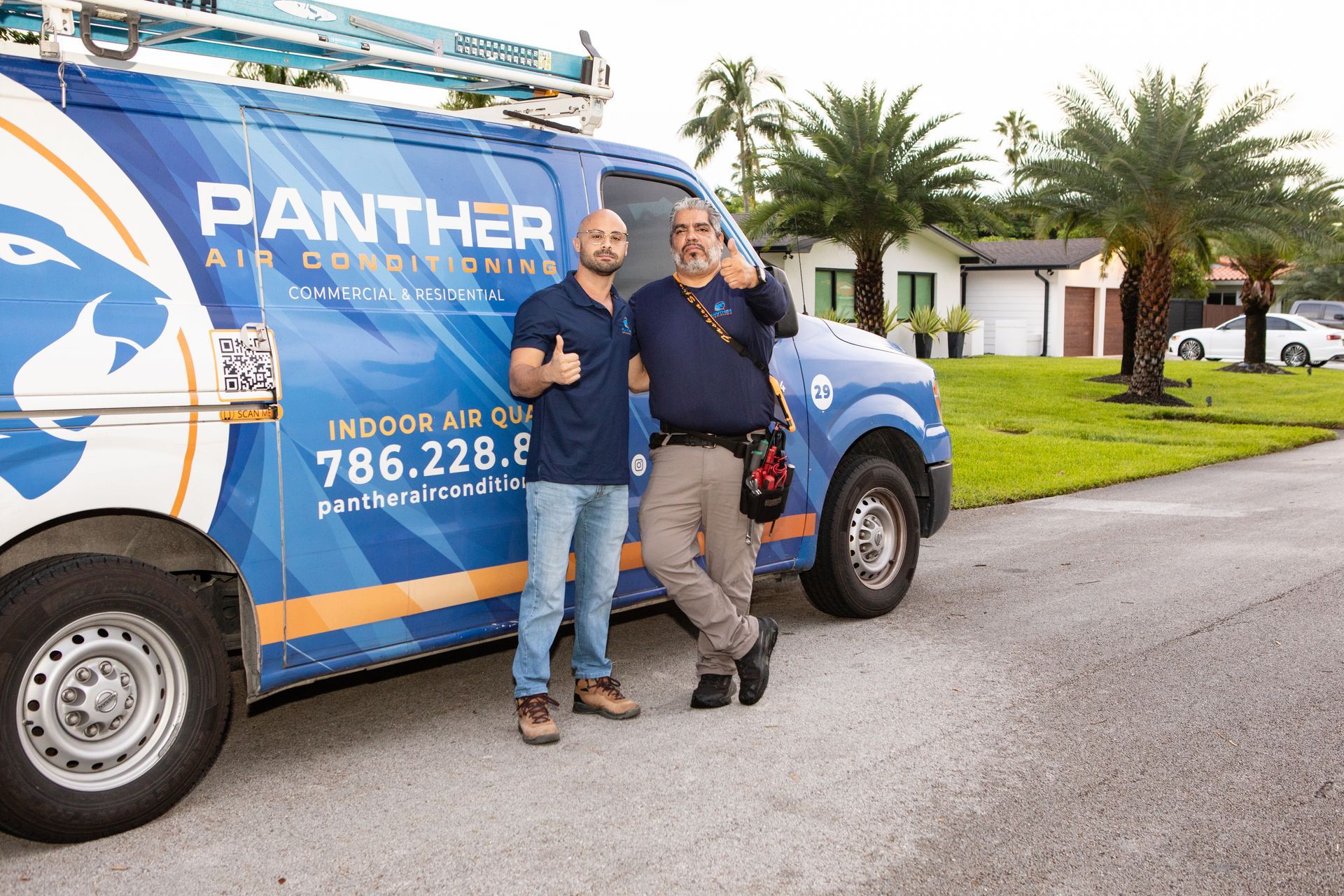 Two smiling people stand beside a blue Panther Air Conditioning van on a suburban street.