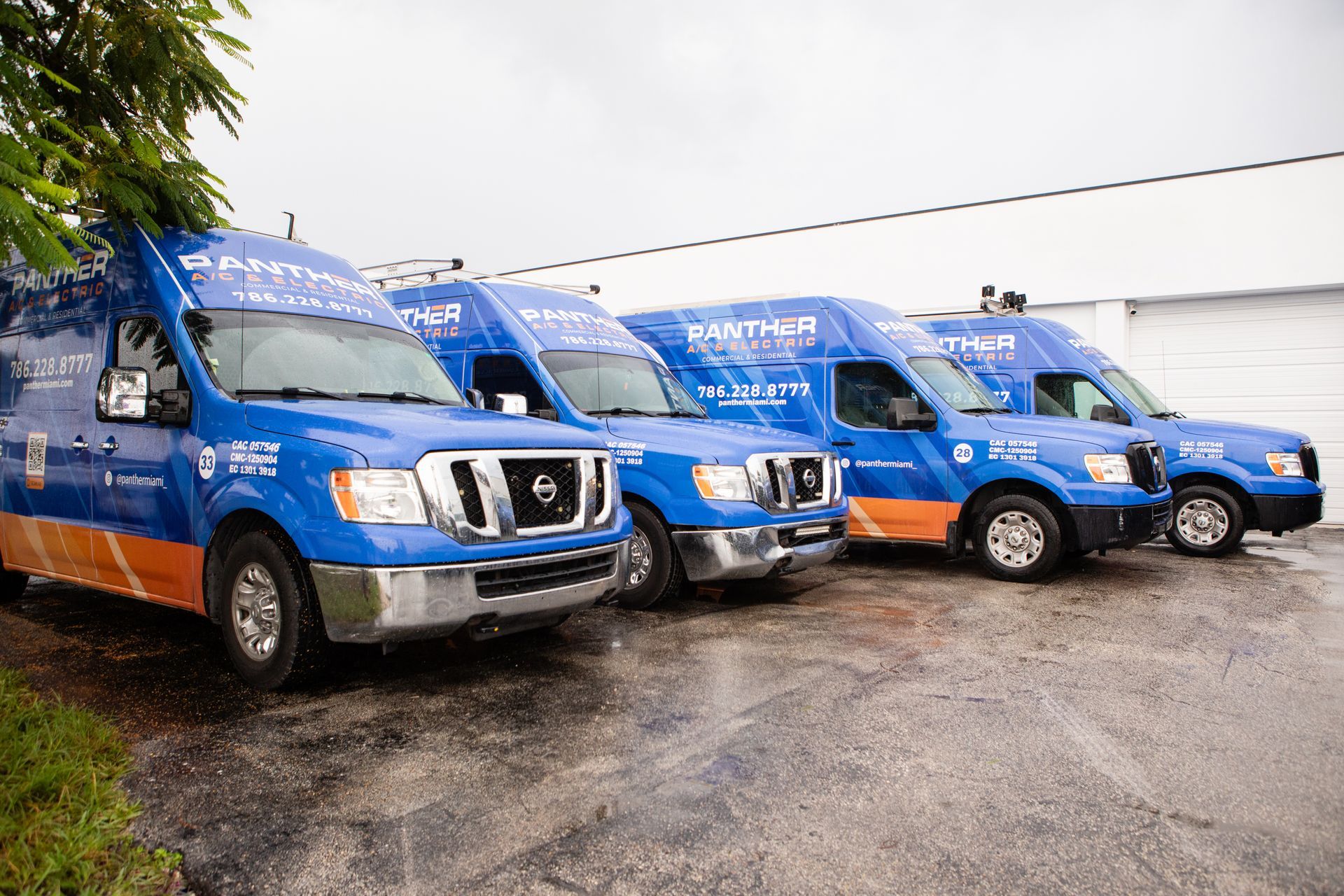 Three blue utility vans parked in a wet lot on a rainy day