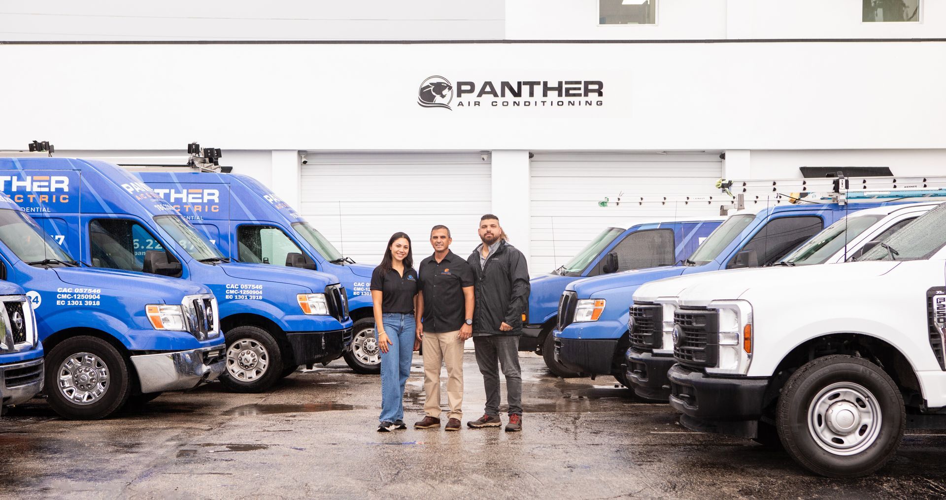 Two people standing between blue and white service trucks in a garage, with a Panther logo behind them.