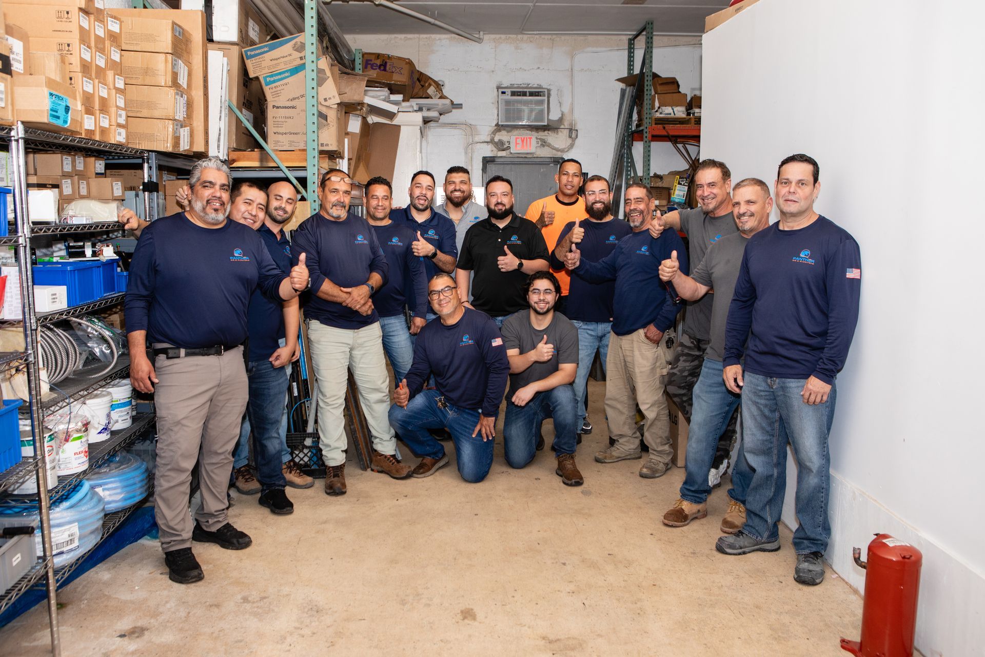 Warehouse staff posing together among shelves and boxes, many in navy shirts, in a storage room.