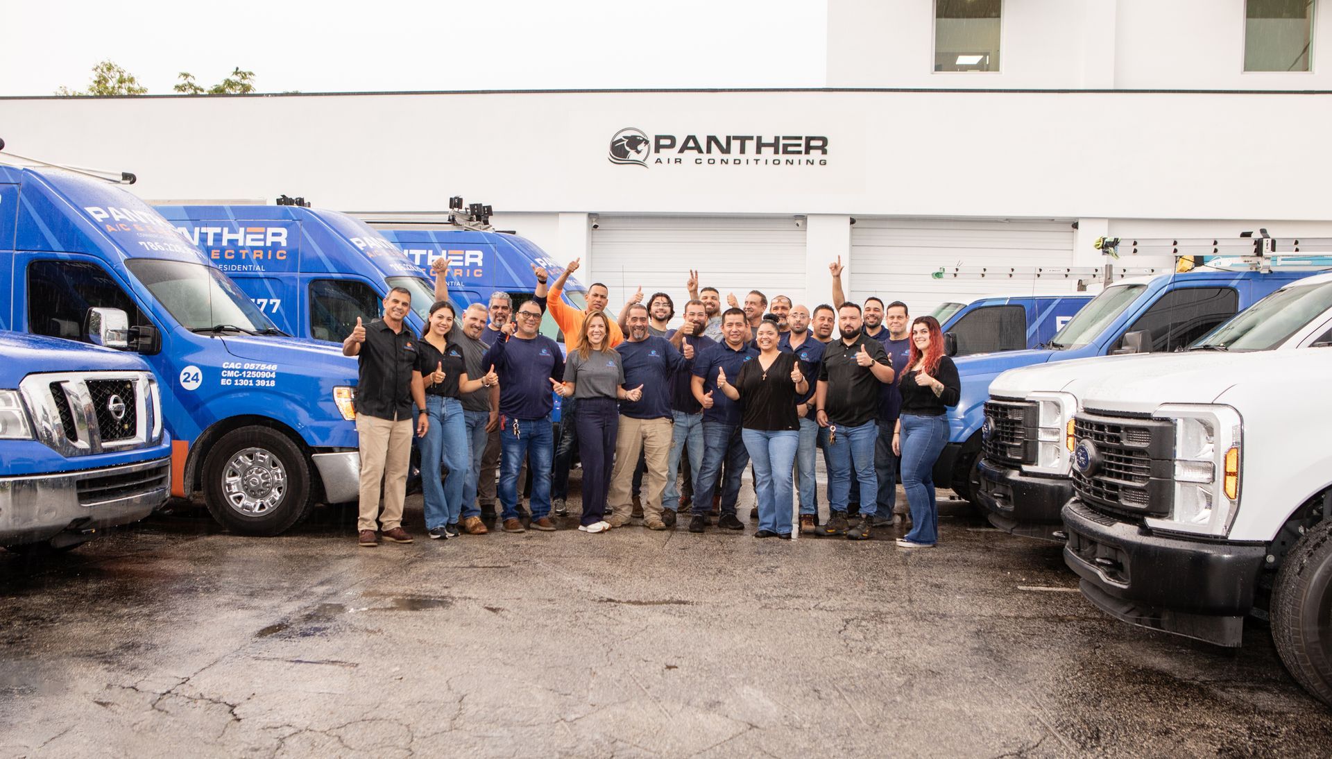 Group of mechanics posing in a garage between blue and white service trucks, with a Panther sign overhead