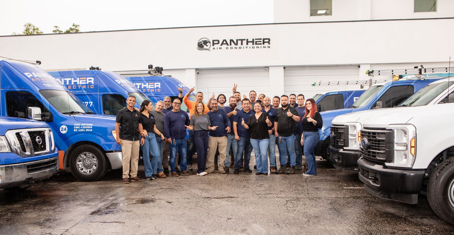 Group of employees posing between blue and white Panther tow trucks in a garage.