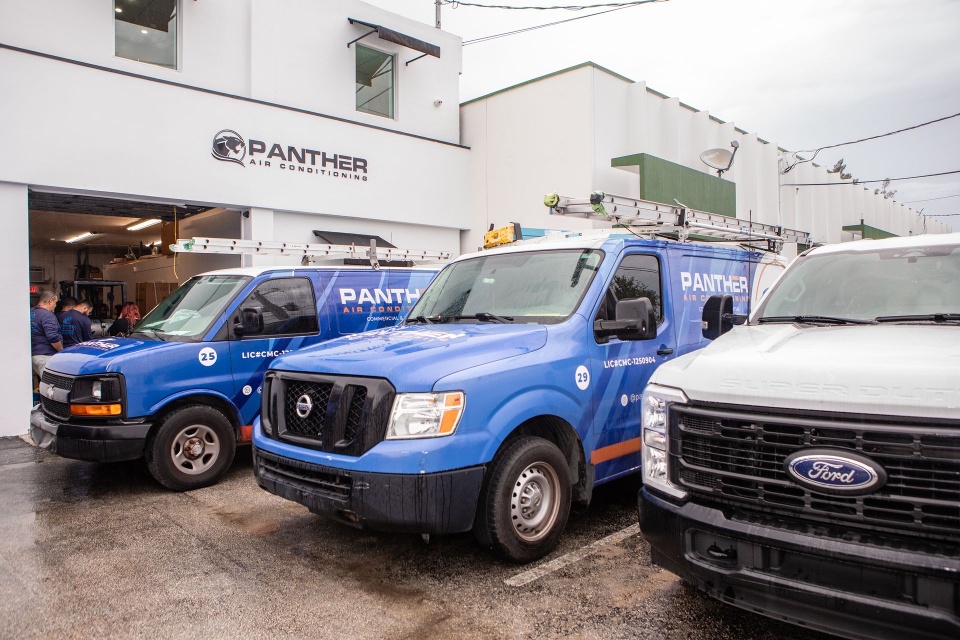 Blue delivery vans parked outside a Panthar dealership in rainy weather