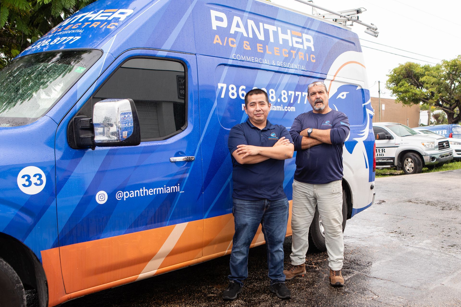 Two men stand beside a blue Panther moving van with orange trim in a parking lot.