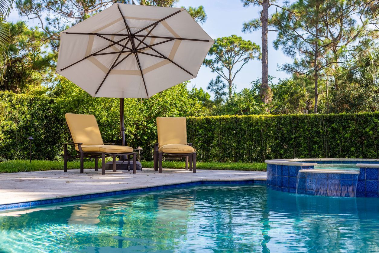 A swimming pool with a white umbrella and chairs around it.