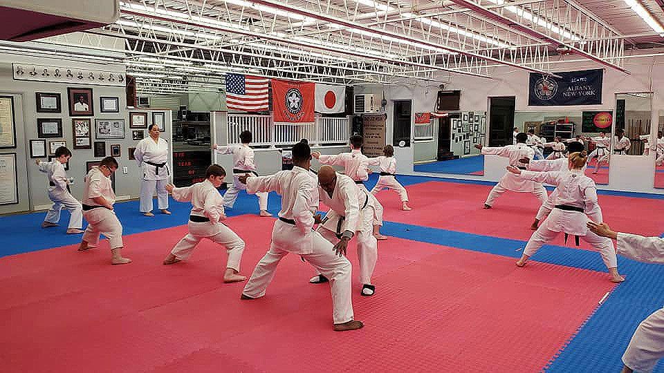 Martial arts class practicing stances on red mats in a dojo with flags on the wall