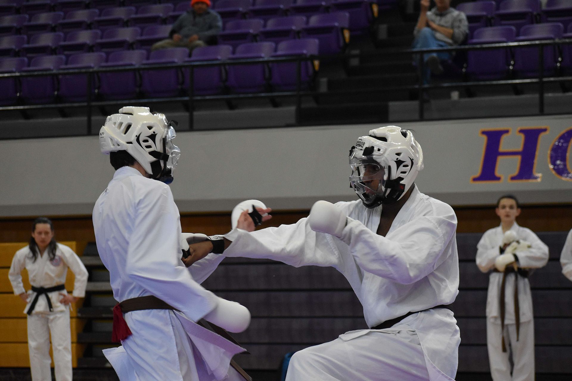 Two martial artists grappling on blue mats, one in a white gi pinning the other.