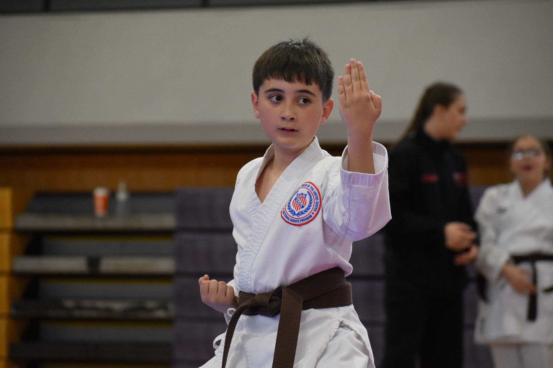 Children in white karate uniforms practicing martial arts in a dojo, one with a blue belt and others behind her