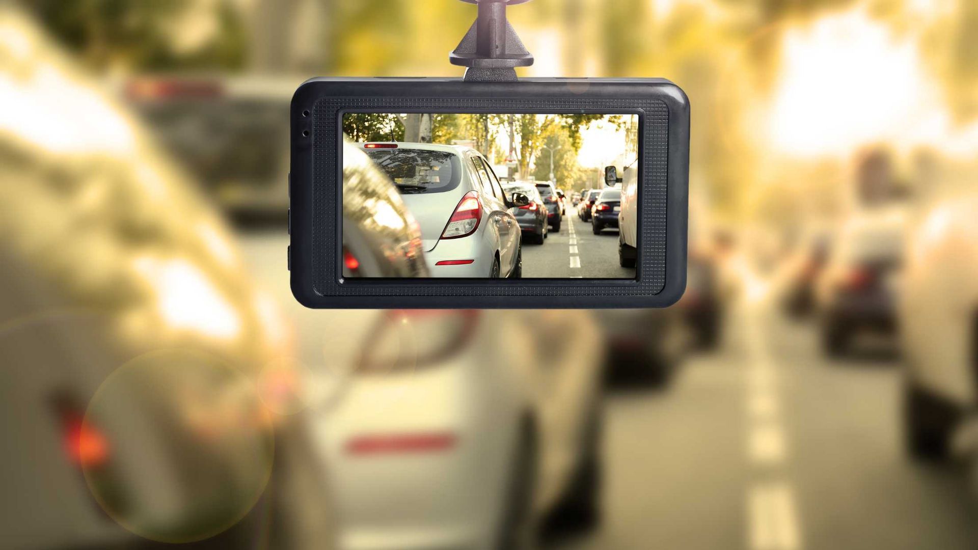 A dash cam is hanging from the rear view mirror of a car.