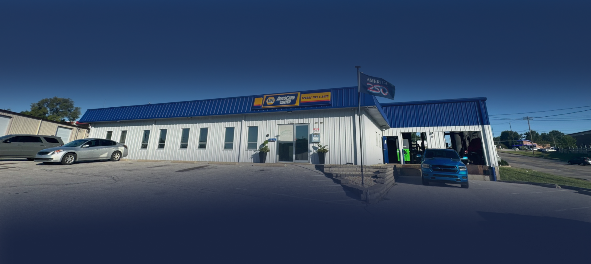 Street view of a blue-roofed commercial building with parked cars on a sunny day | Sparks Tire & Auto