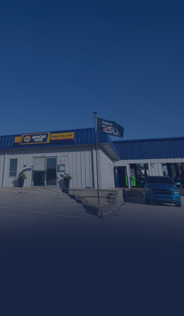 Three people stand beside cars in front of a blue warehouse on a sunny day. | Sparks Tire & Auto