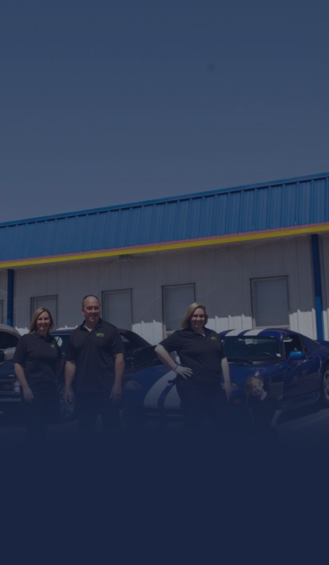 Three people stand beside cars in front of a blue warehouse on a sunny day. | Sparks Tire & Auto
