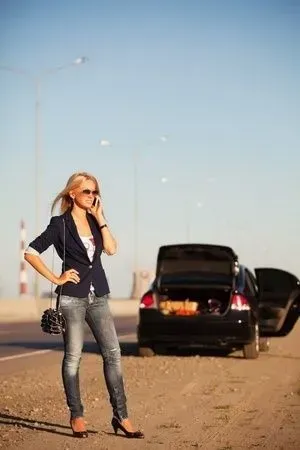 Woman in sunglasses standing by a car on a roadside, talking on a phone with trunk open. | Sparks Tire & Auto